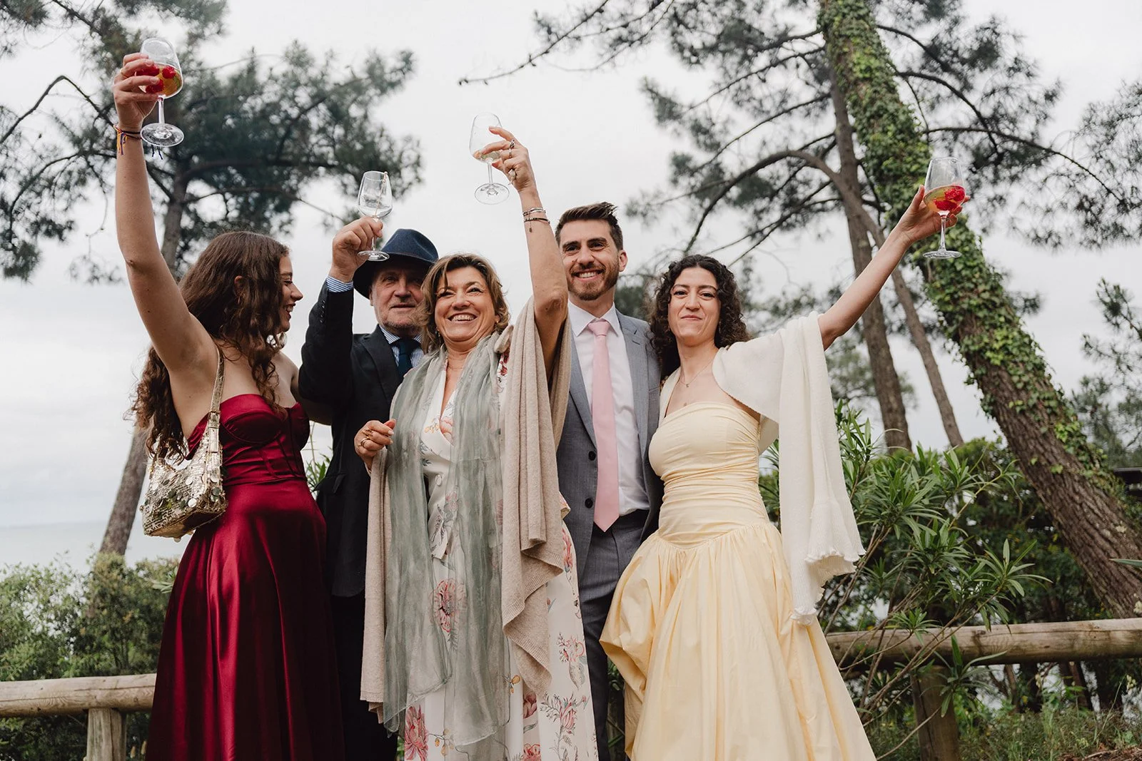 Groupe de personnes souriantes tenant des verres lors d'une célébration en plein air, avec des arbres en arrière-plan.