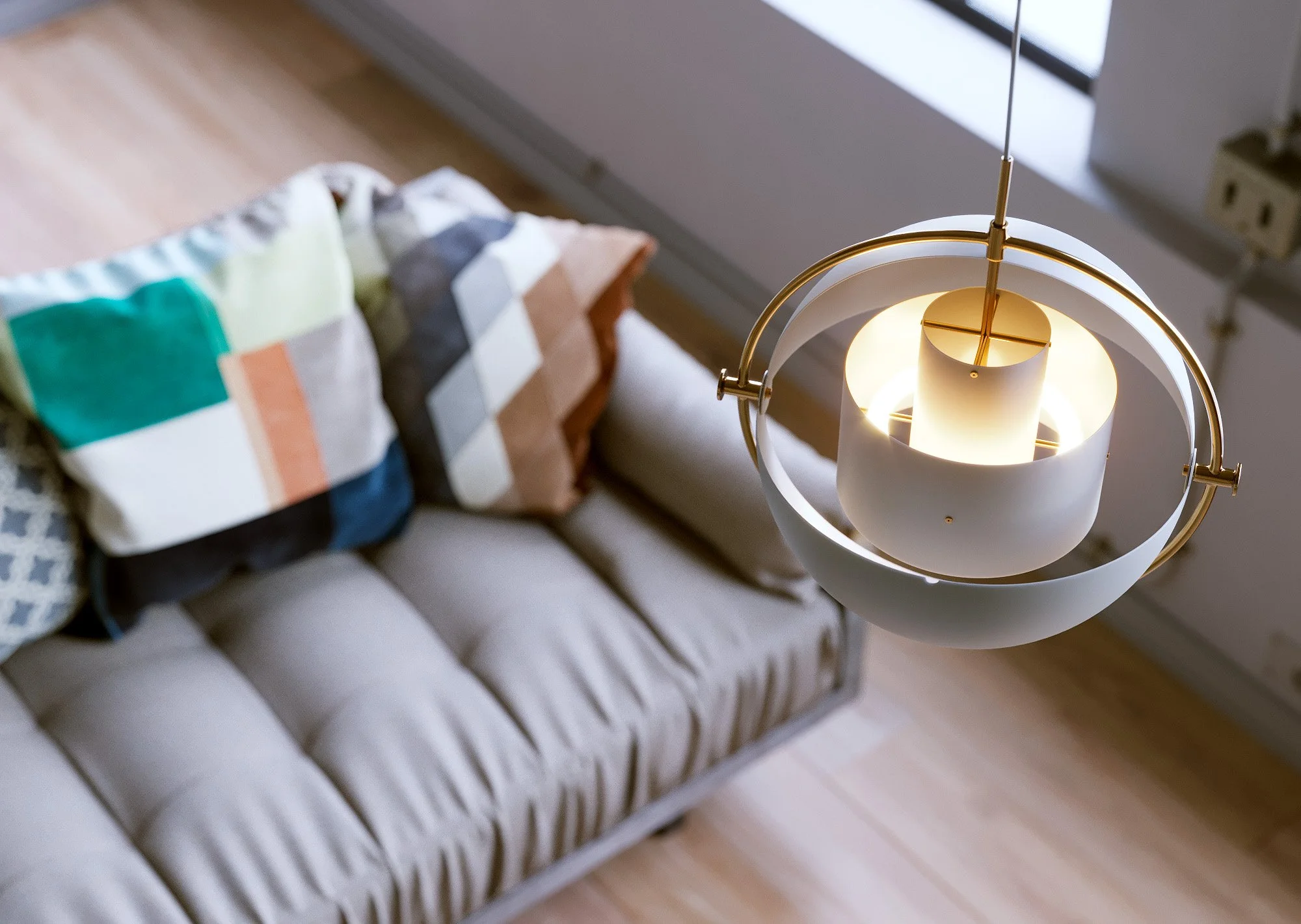 A beige sofa with three decorative pillows and a modern ceiling lamp hanging above in a room with wooden flooring.