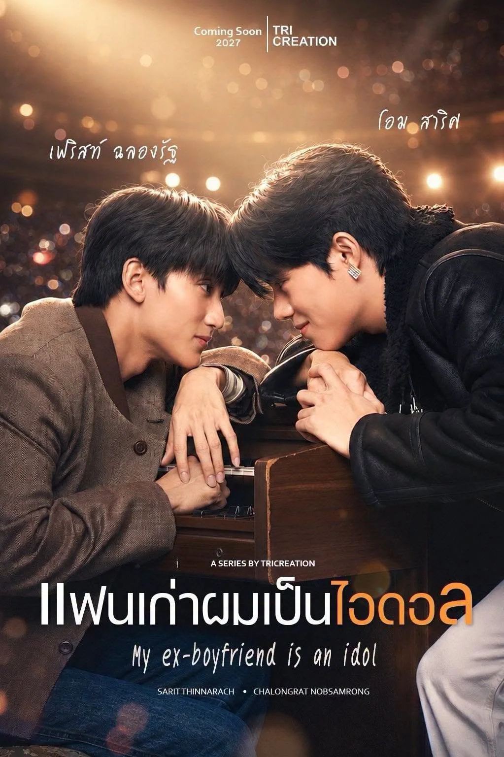 Two young men are touching foreheads and looking into each other's eyes with a castle wall in the background. They are leaning on a piano, and both are wearing stylish jackets.