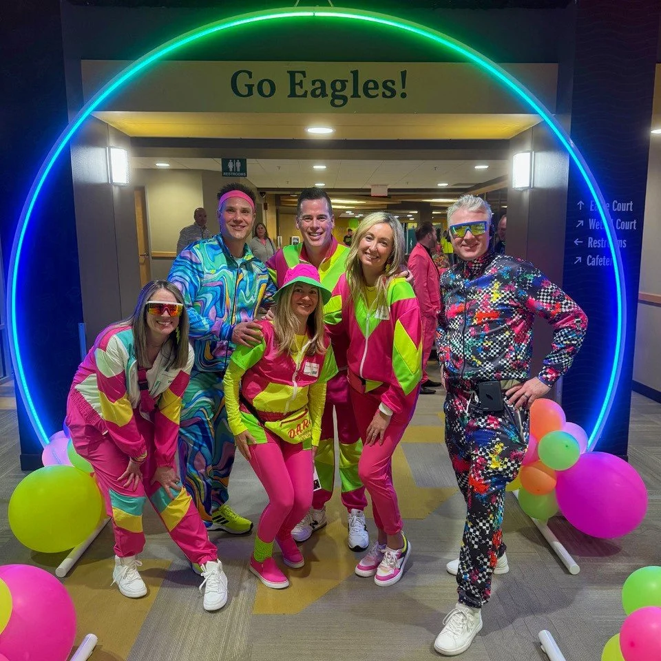 group dressed in neon clothing standing under a neon orb at auction event