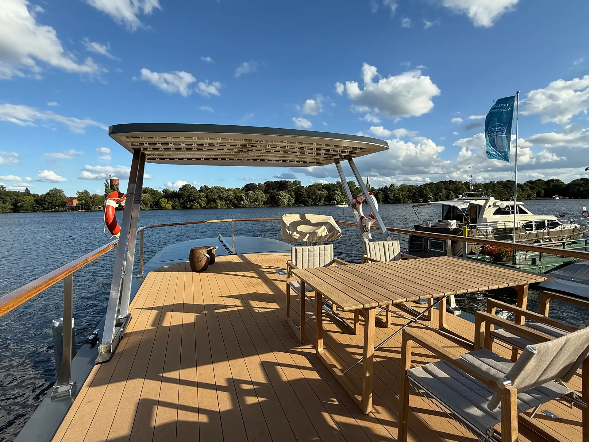Auf der Terrasse eines Bootes mit Blick auf den Fluss, inklusive Tischen und Stühlen, unter einem blauen Himmel mit Wolken.