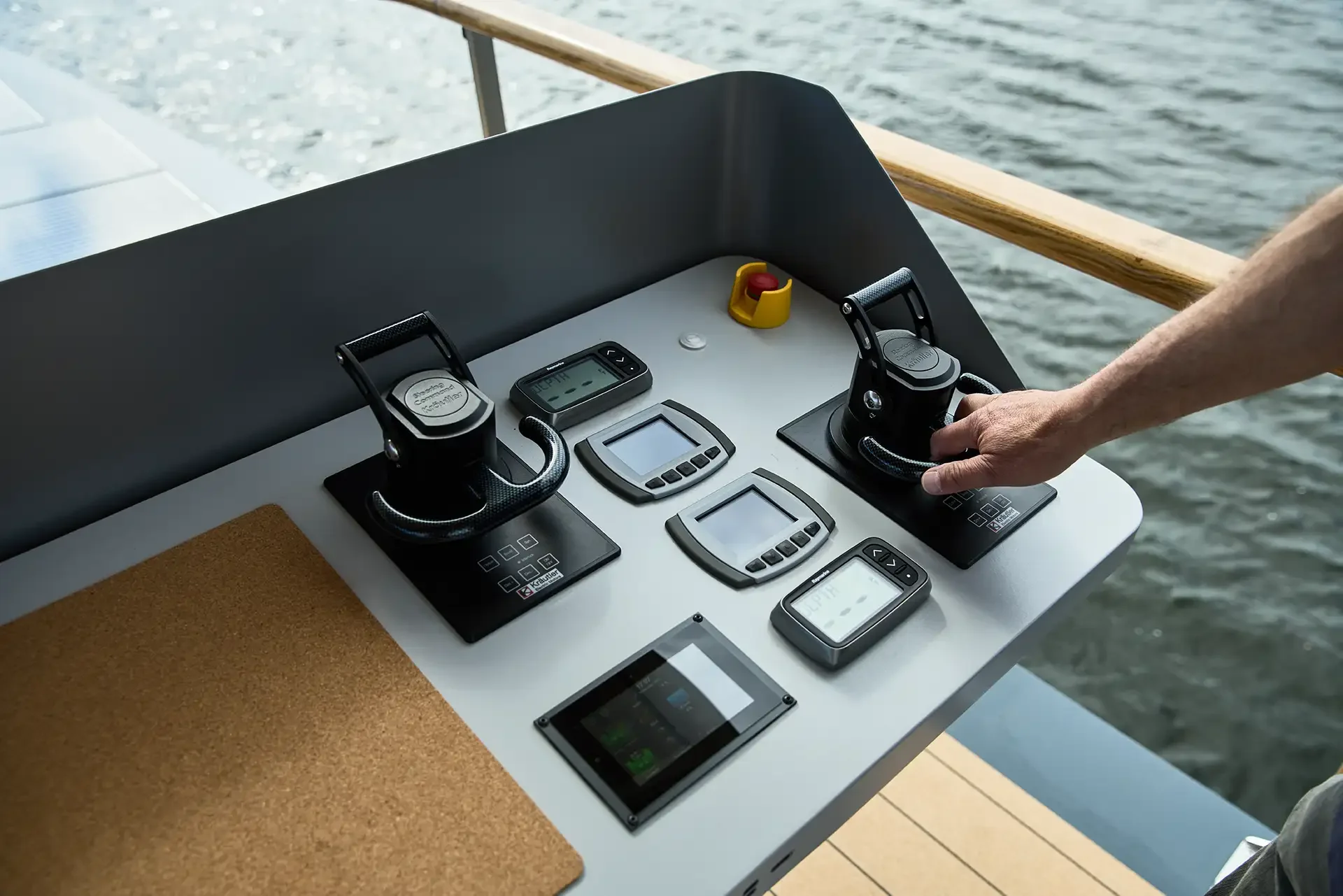Steuerstand einer Yacht mit zwei Joysticks, Navigationsgeräten und einem Feuerlöscher, Blick auf Wasser im Hintergrund.
