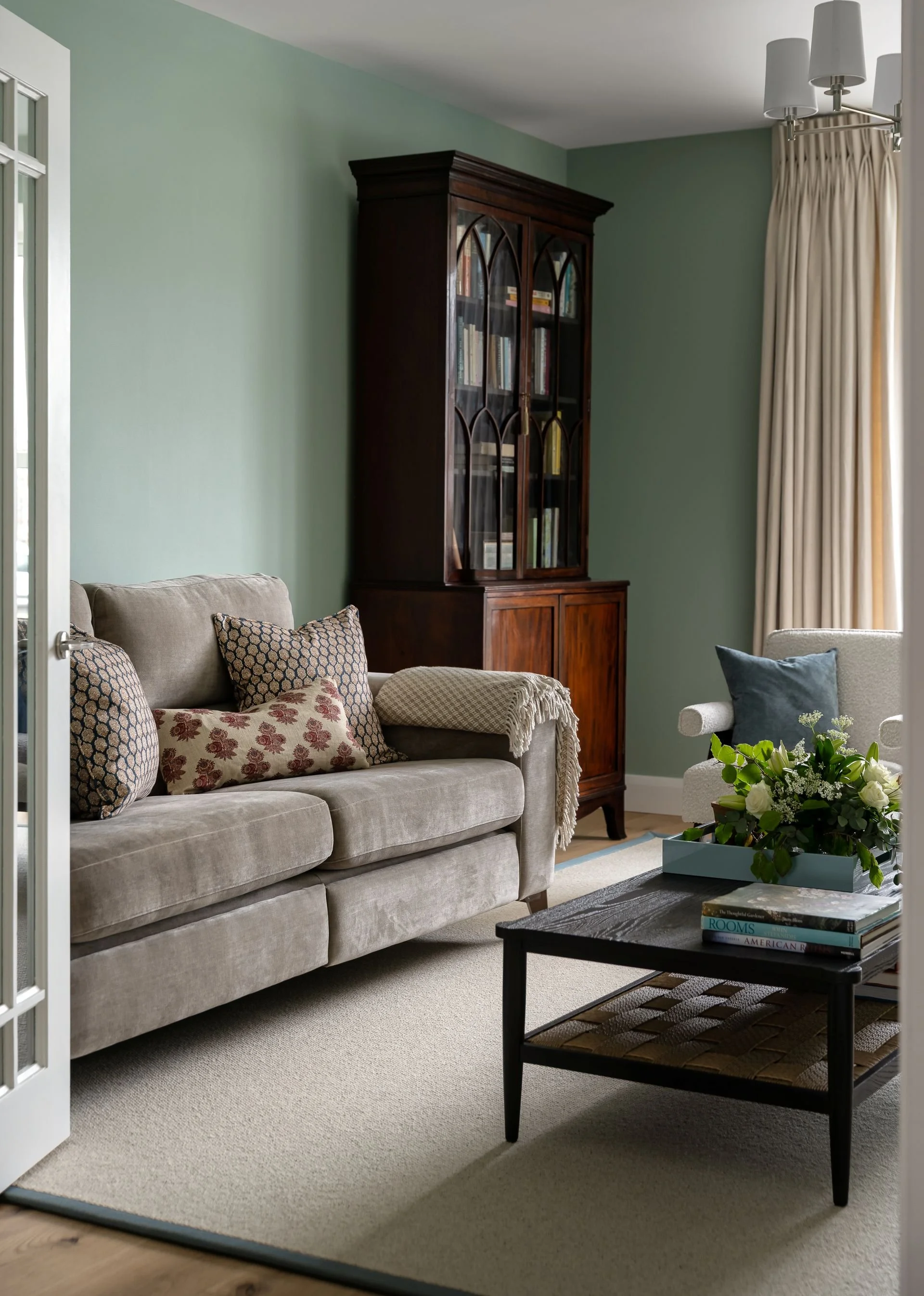 Elegant green sitting room with antique bookcase, patterned cushions and full-length curtains by South Hill Studio in Kilkenny.