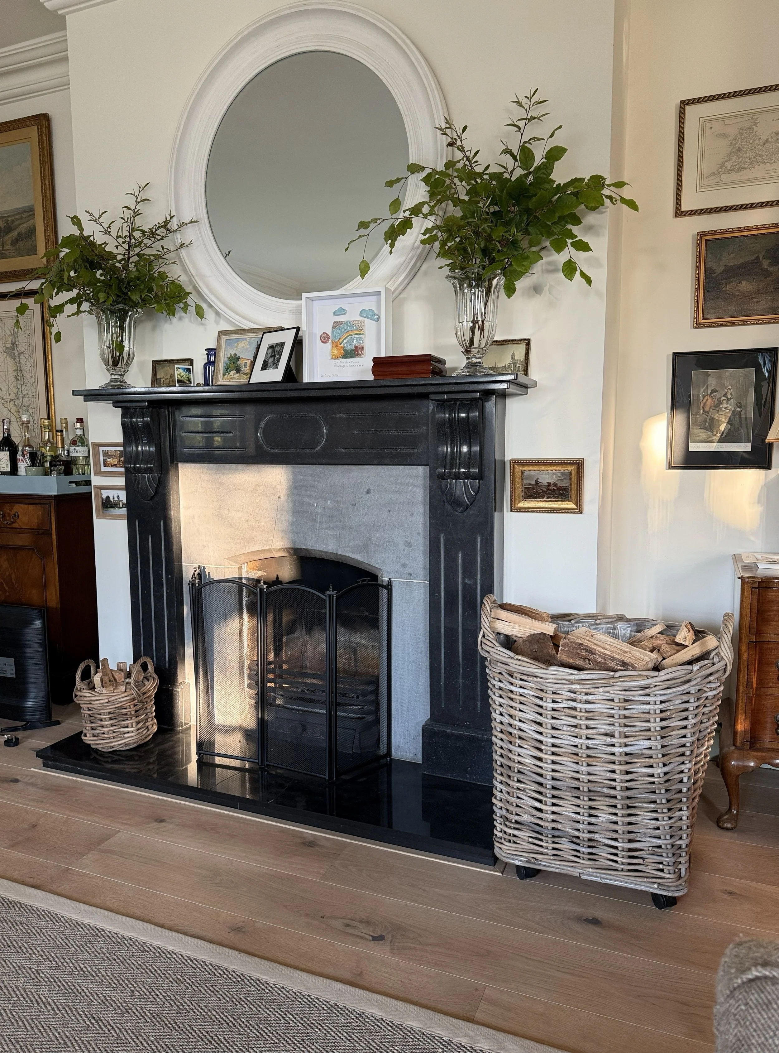 Traditional black marble fireplace with antique artwork, layered framed prints and fresh greenery, styled in a classic Kilkenny country home interior.