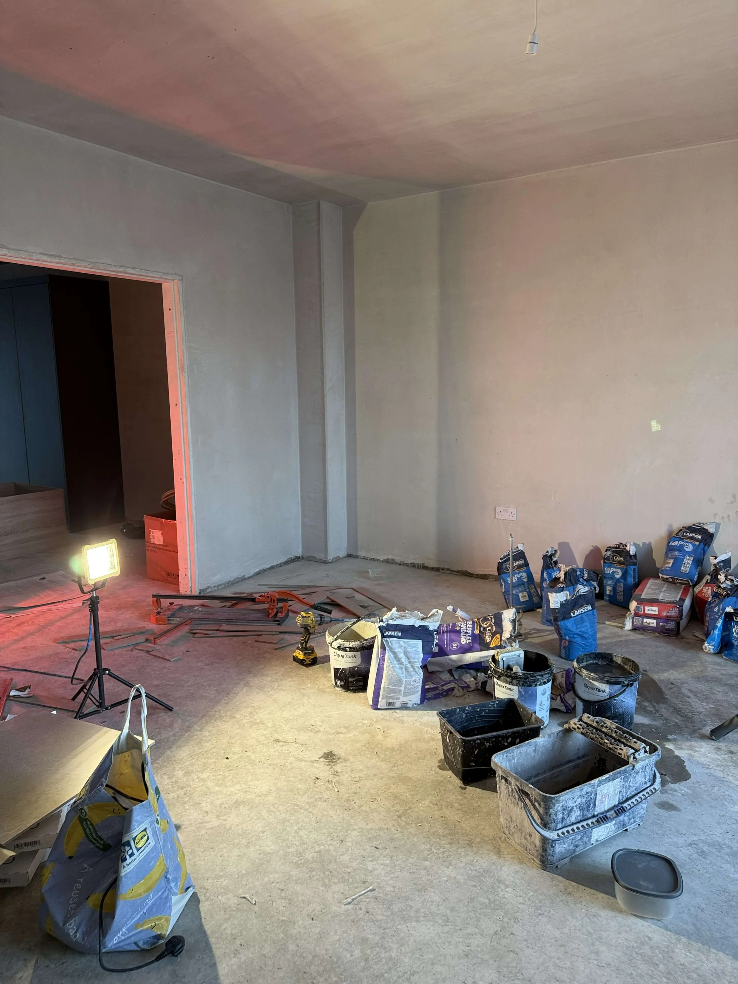 Before view of a new-build living space during construction, with plastered walls, unfinished flooring and building materials on site