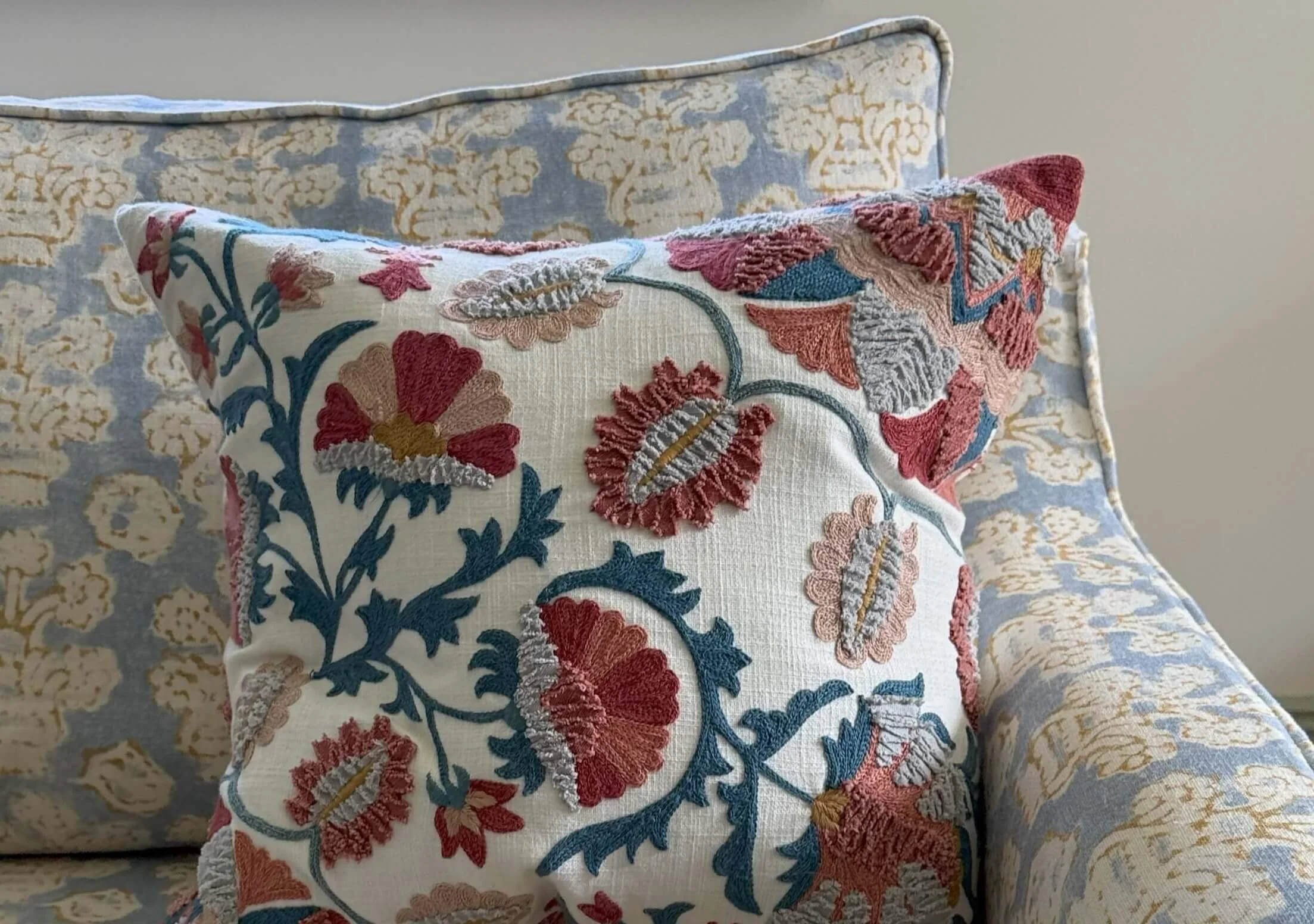 Close-up of decorative pillows with intricate floral embroidery on a blue and cream patterned couch.