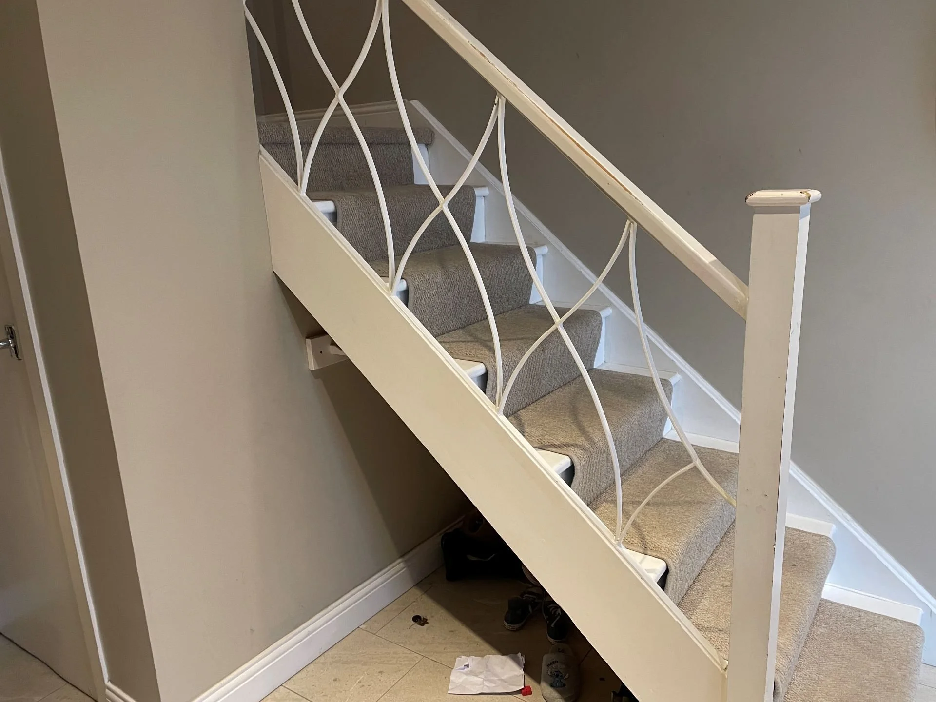 A staircase with beige carpet and a white metal railing with decorative curves, positioned next to a gray wall and a white door.