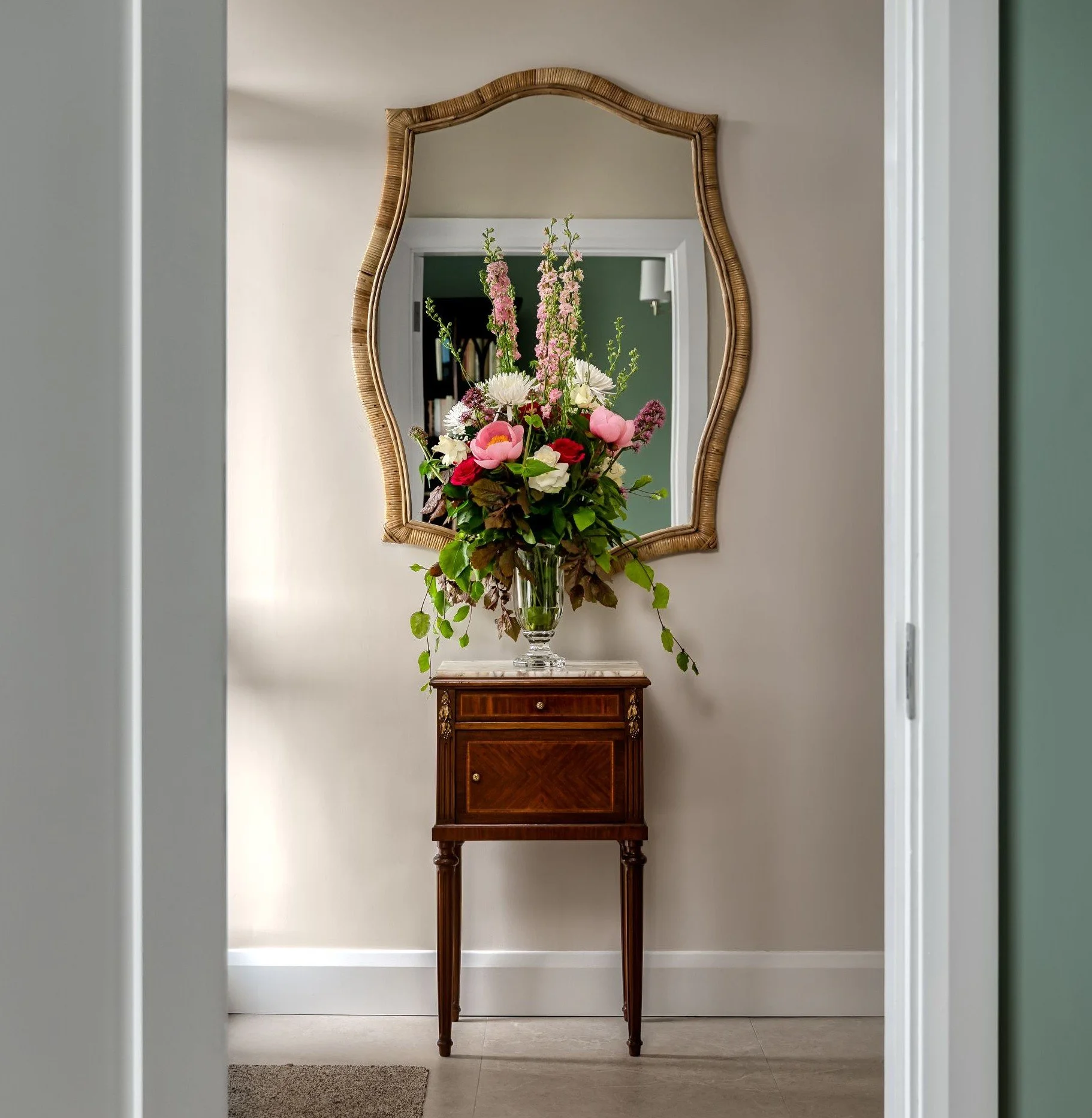 Warm hallway with stone flooring, antique French chest and rattan-wrapped mirror.