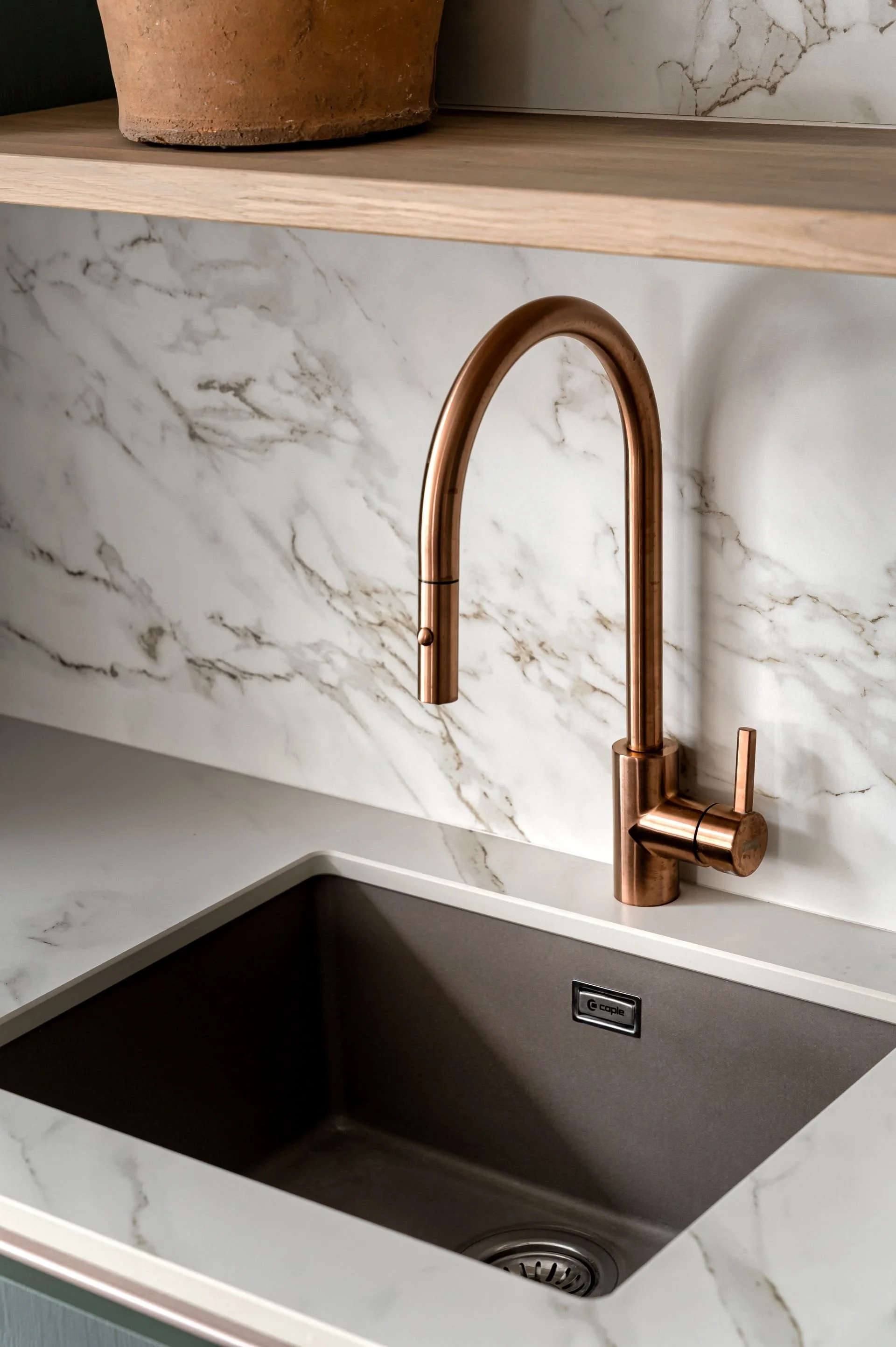 Elegant copper kitchen tap with spray nozzle, marble countertops and backsplash.
