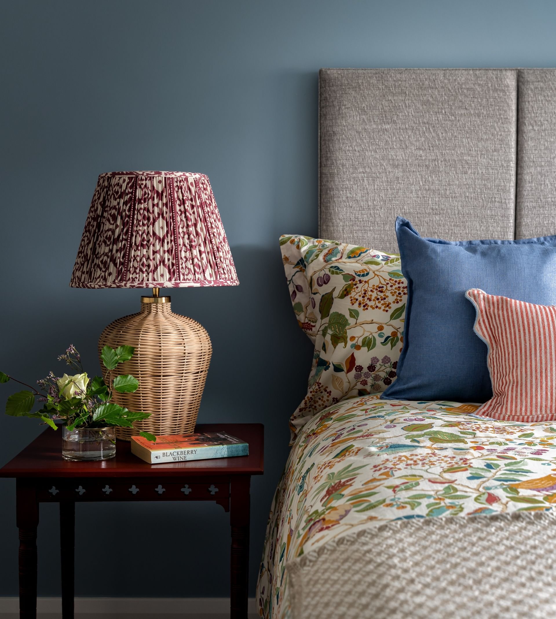 Colourful bedroom with wicker lamp, antique table and blue walls.