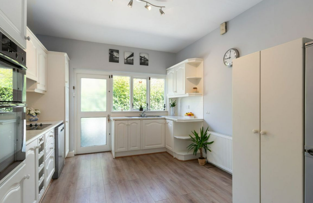 Bright kitchen with white cabinets, a window over the sink, a potted plant on the floor, and a door leading outside.