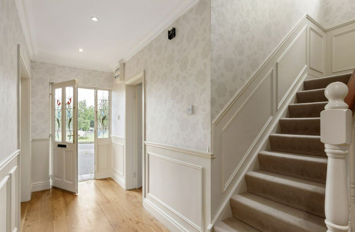 Entryway with open front door, stained glass panels, hardwood floor, wall paneling, and carpeted staircase.