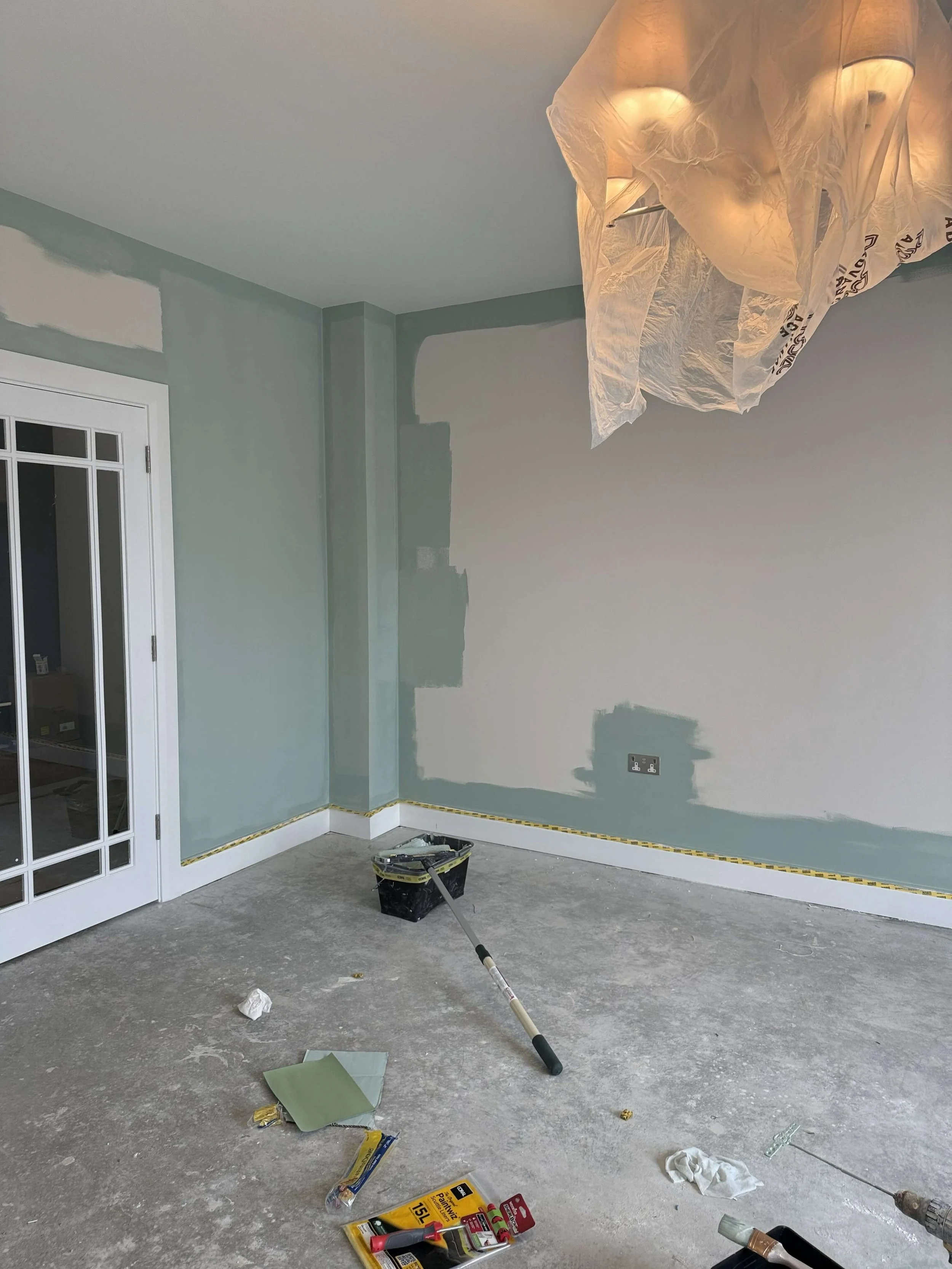 New-build living room in Kilkenny during the painting stage, with soft green walls, unfinished flooring and lighting protected for decorating.