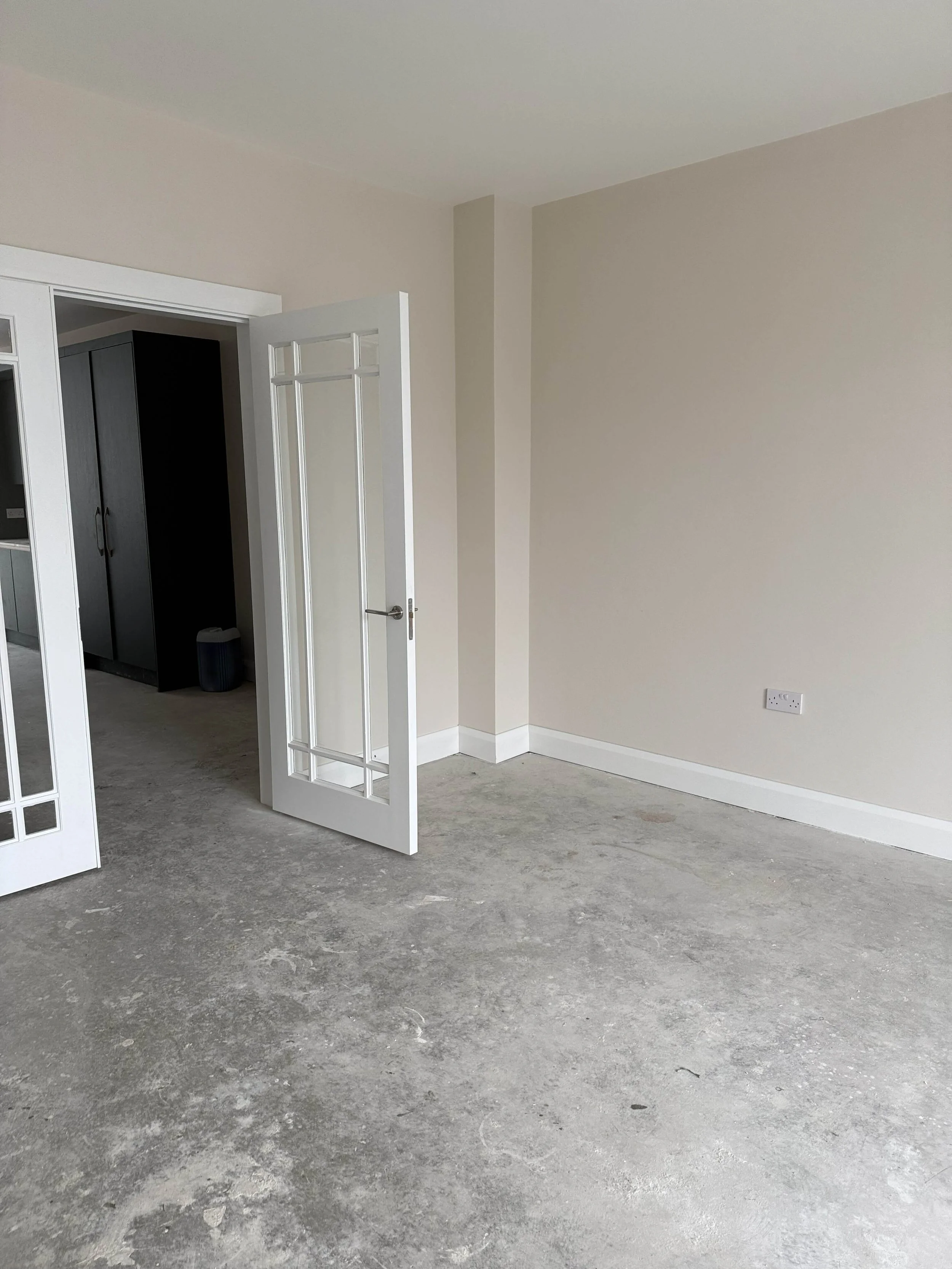 New-build living room in Kilkenny with the builder’s standard paint finish, glazed double doors and unfinished concrete floor before the final interior colour scheme and flooring were installed.