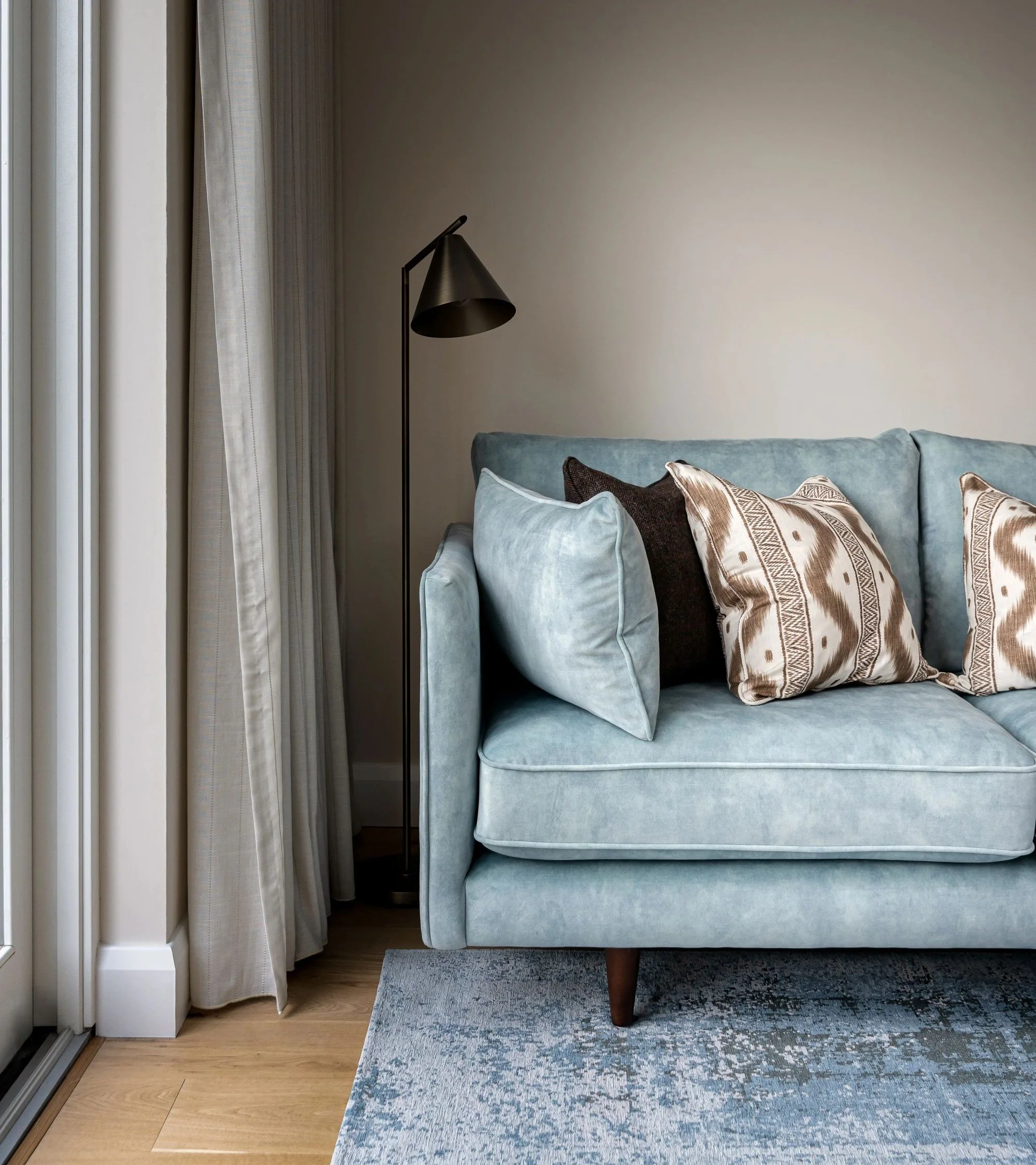 Pale blue sofa with wool and textured linen cushions and bronze reading light.