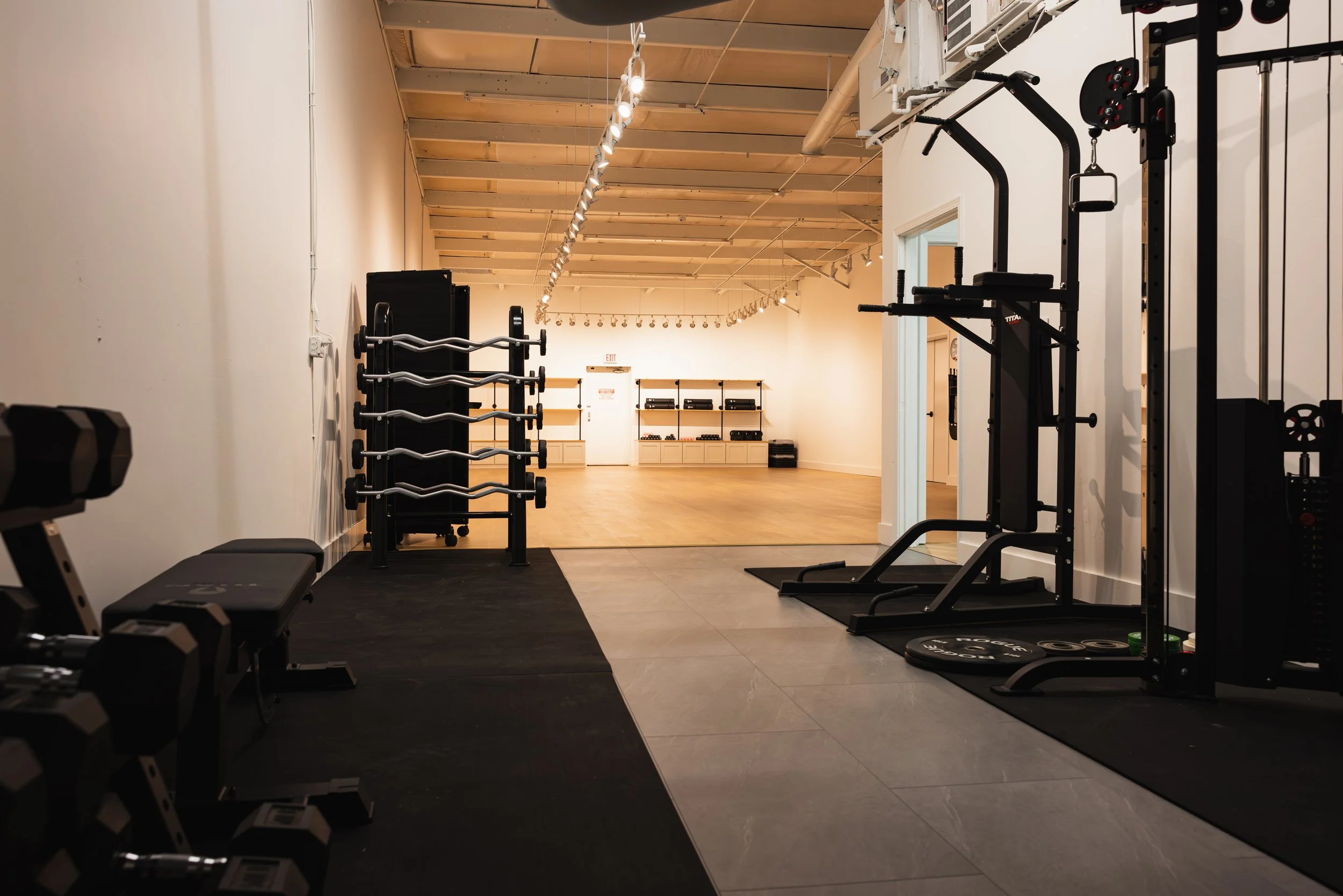 Empty gym with weight racks, resistance machines, and hardwood flooring in the workout area.