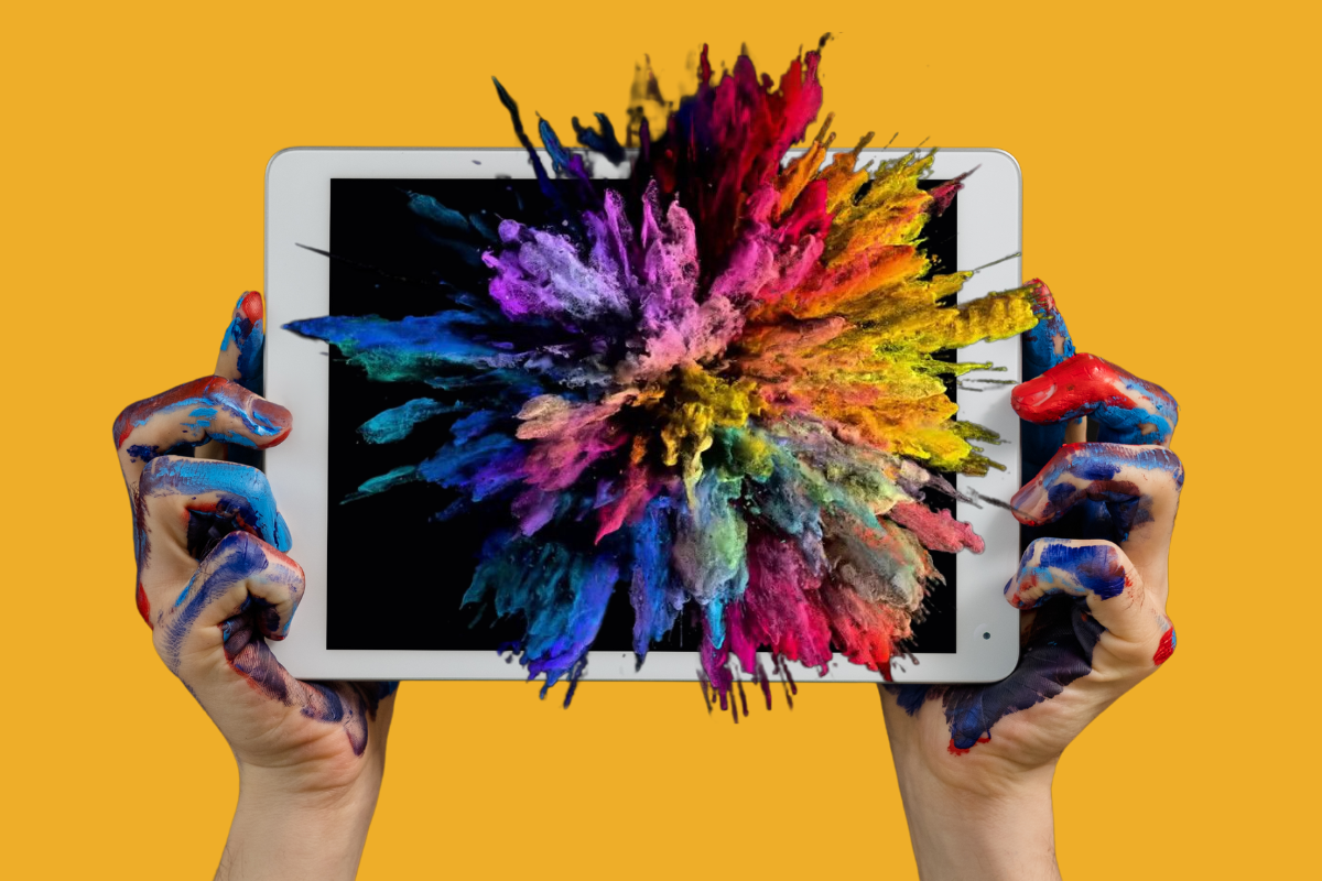 Hands covered in colorful paint holding a tablet with an explosion of vibrant powder colors emerging from the screen, against a yellow background.