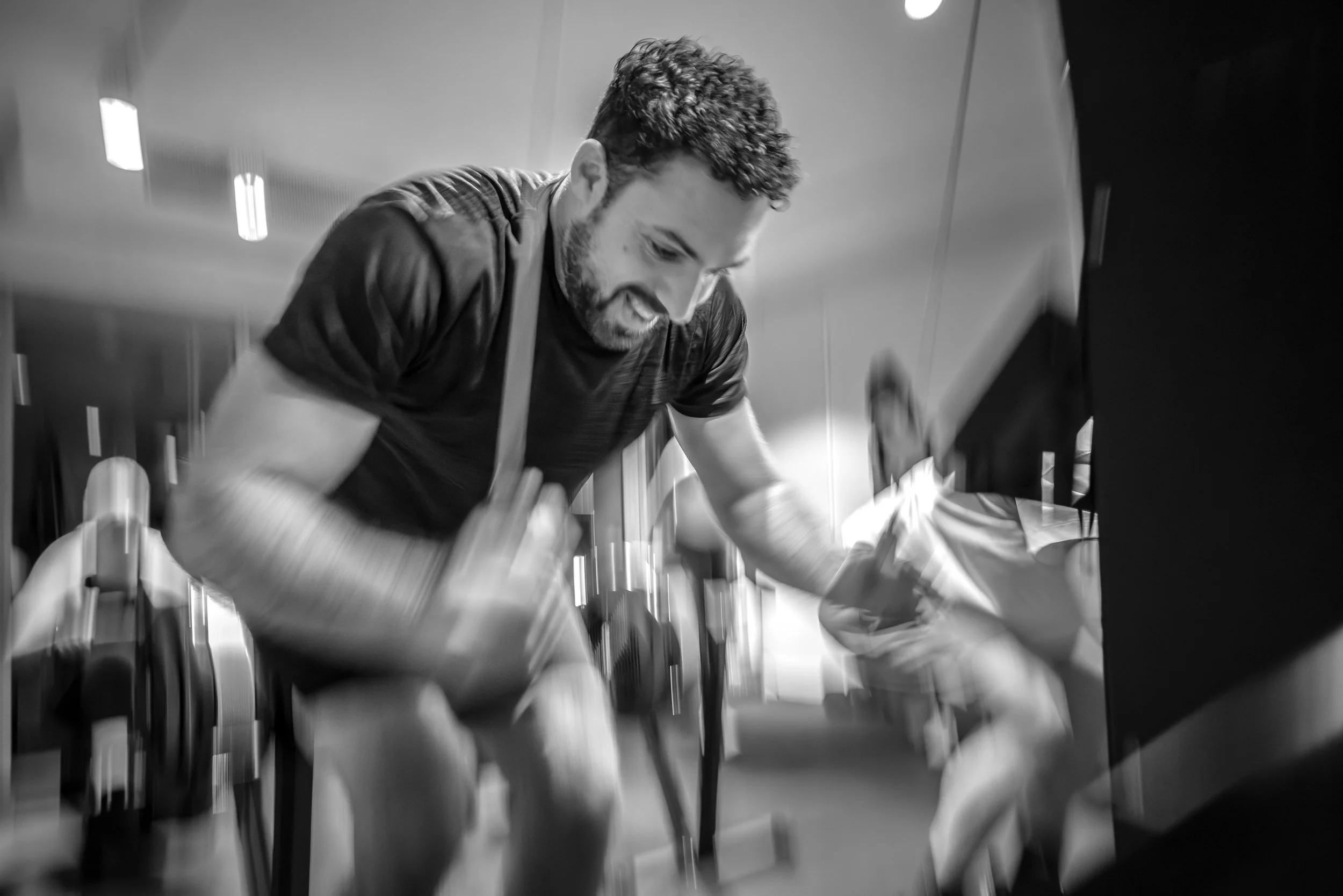 A man with curly hair and a beard, smiling, is playing an indoor piano.