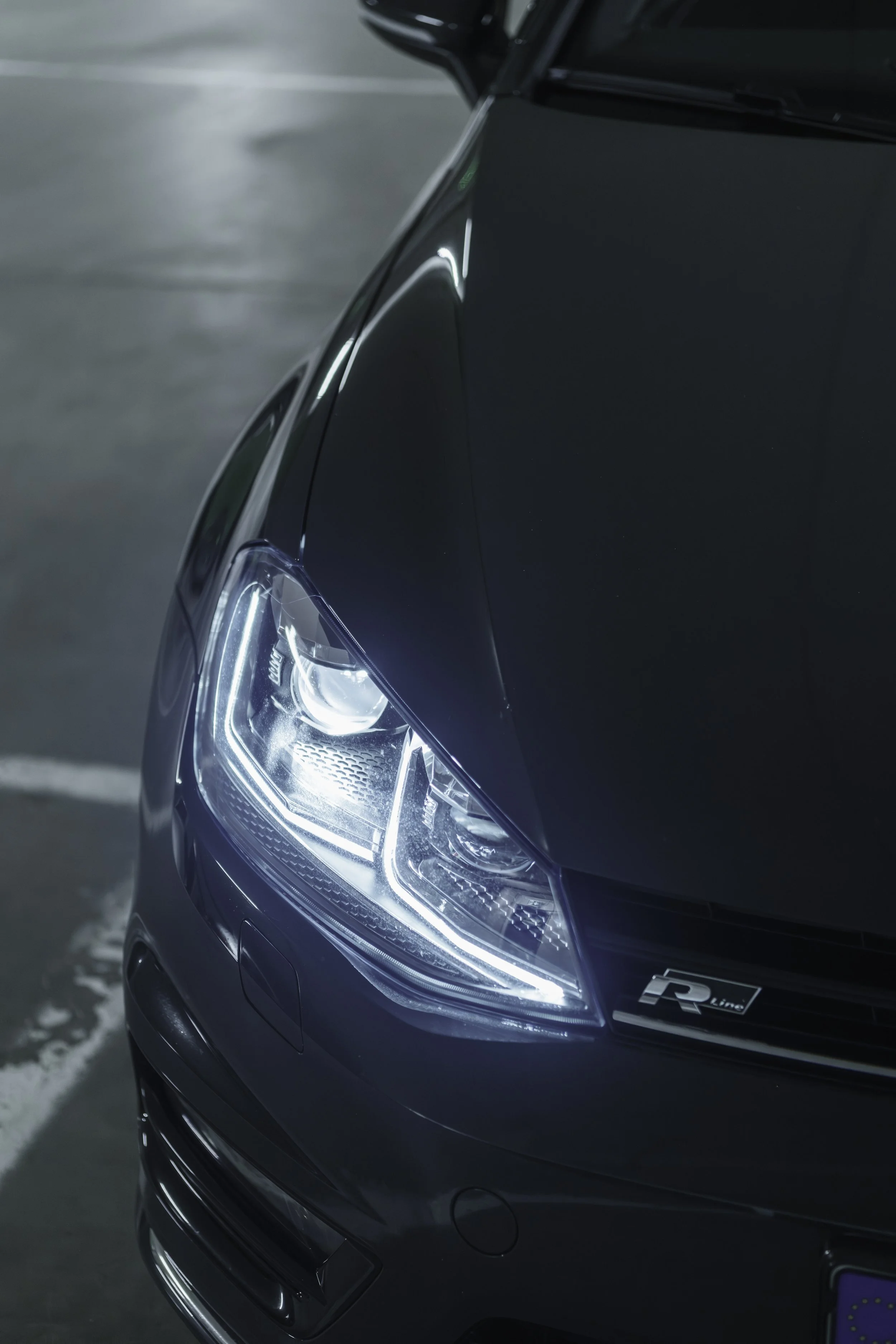 Close-up of the front of a black car with LED headlights in a parking garage.