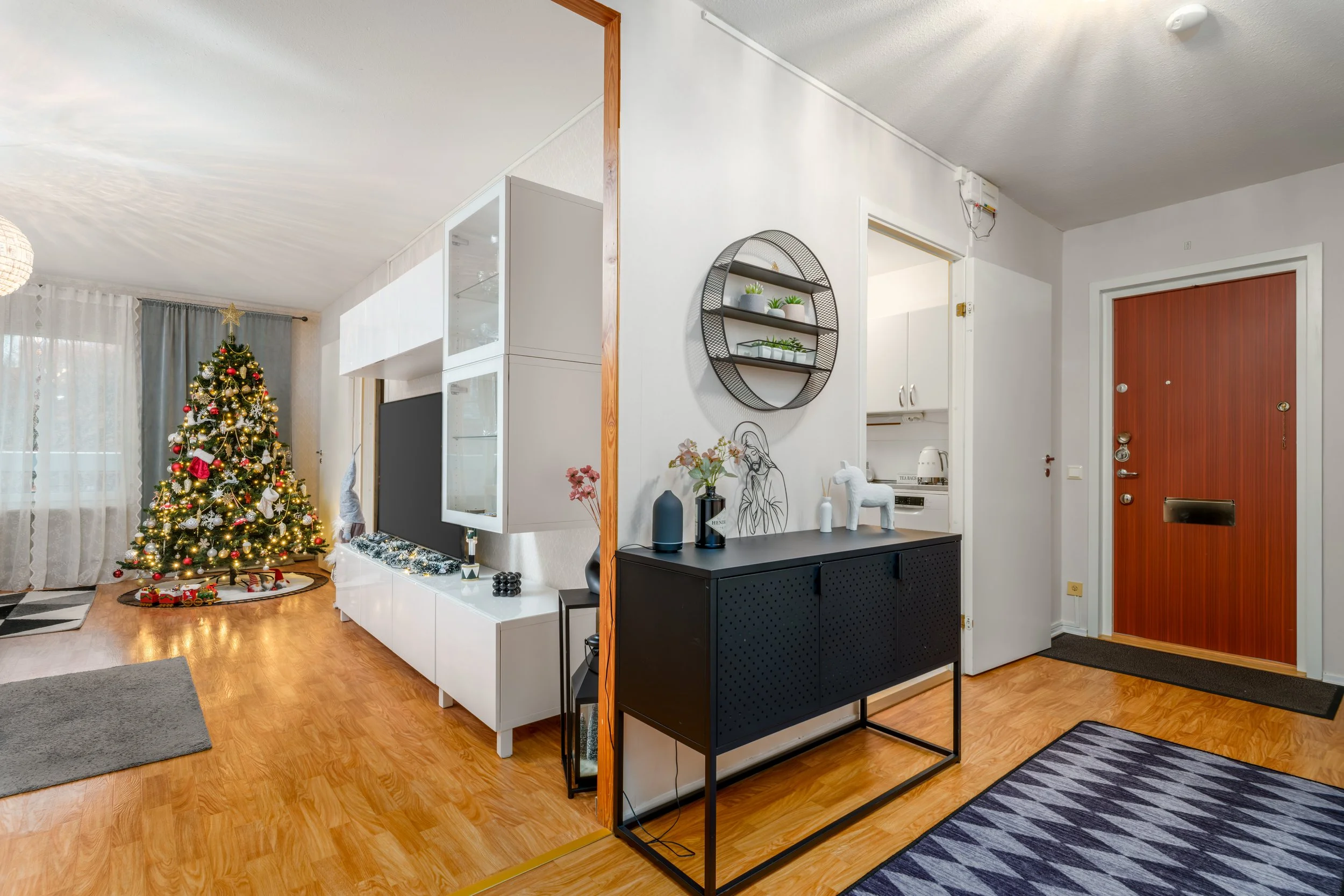 Living room with decorated Christmas tree, white furniture, and a front door.