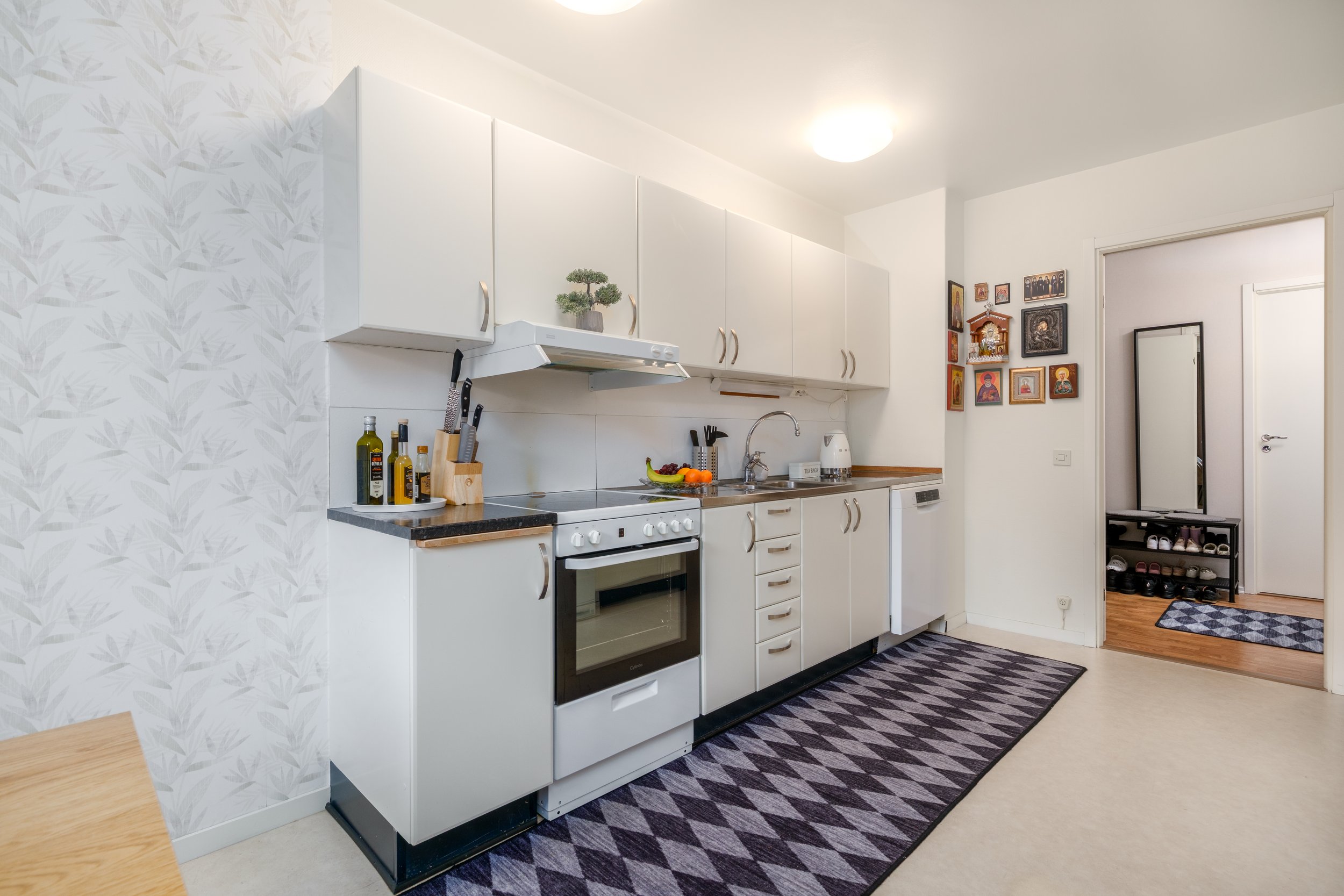Kitchen with white cabinets, black countertop, stove, sink, and fridge, decorated with small plant, bottles, and fruit.