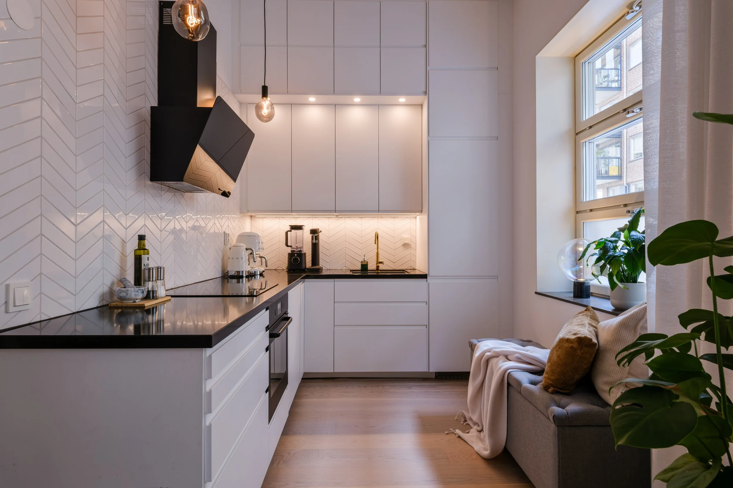 Moody interior photography of a Scandinavian kitchen with white chevron tile, black hood and brass tap, warm under-cabinet light.