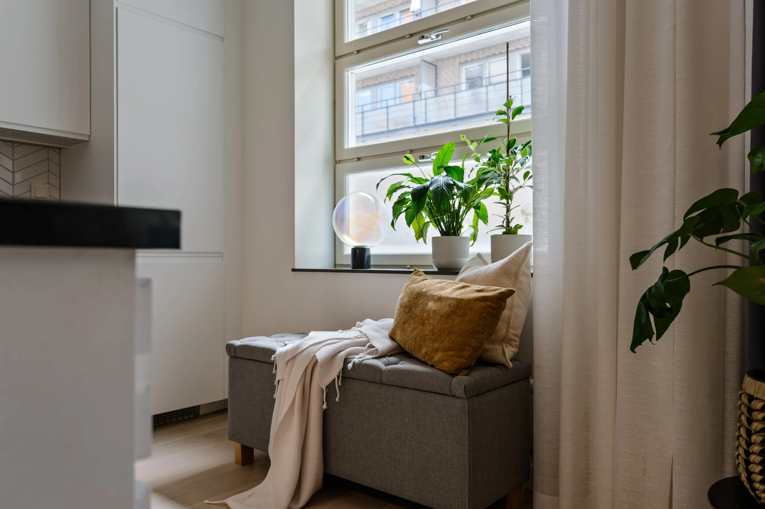 Interior detail photograph of a window reading bench with linen cushions and greenery, soft natural light.