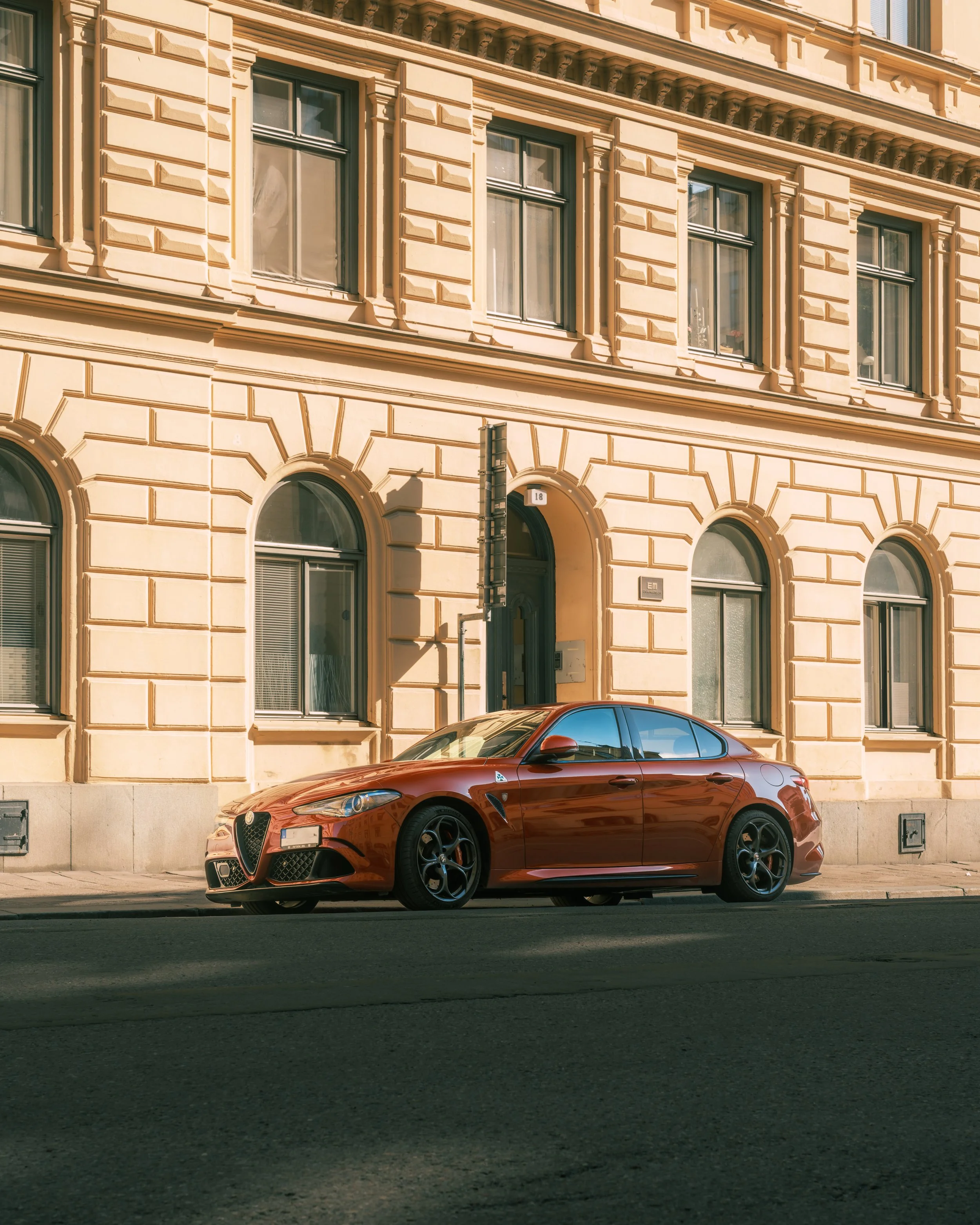 A red sports car parked on the street in front of a historic beige building with ornate architectural details.