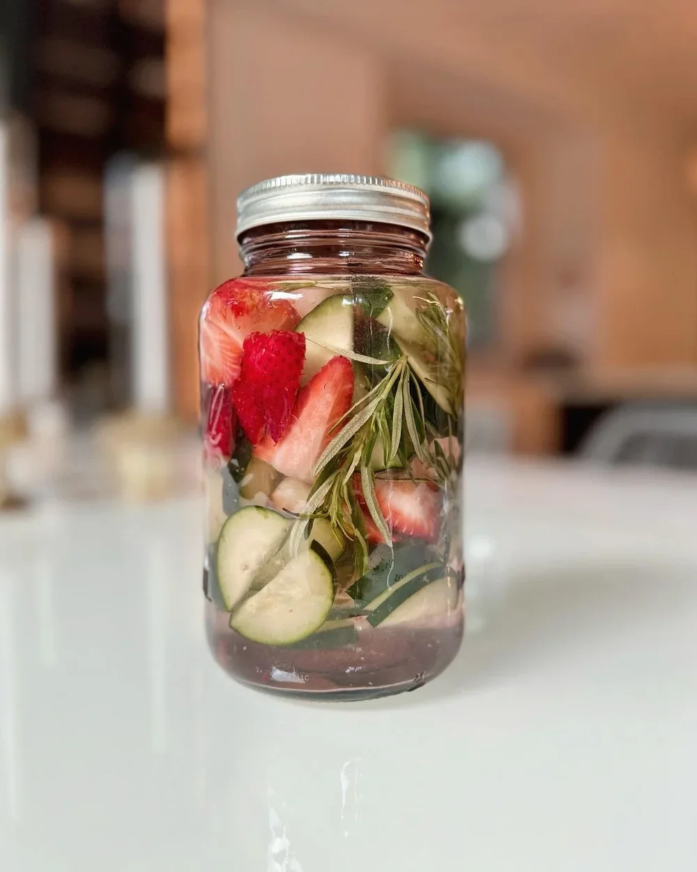 A glass jar filled with sliced strawberries, cucumbers, herbs, and other fruits in spa hydration water.