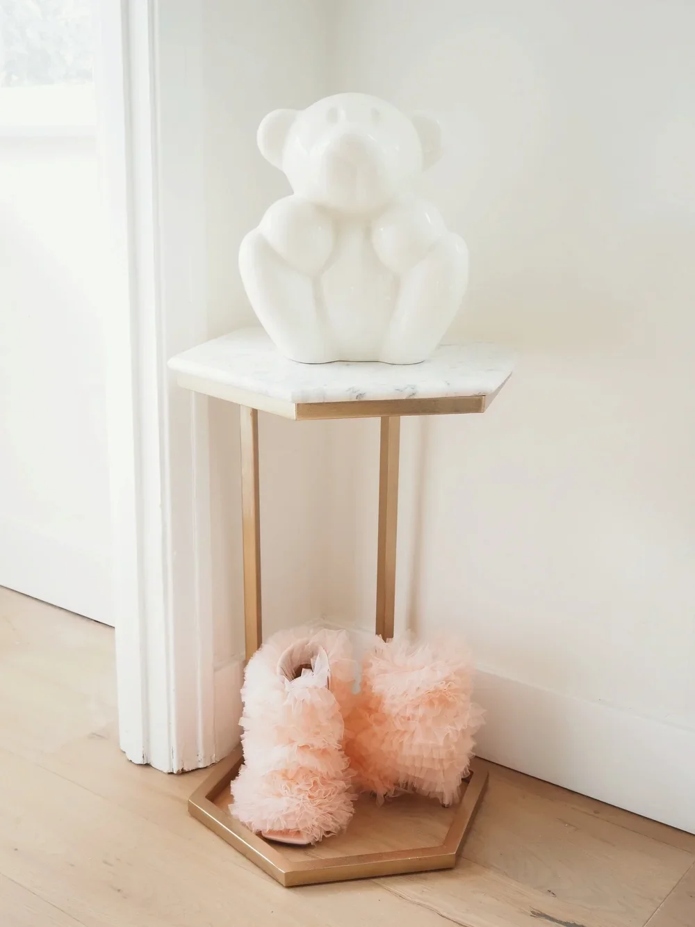 White stuffed animal sculpture on a small table with pink fluffy slippers underneath. Newborn baby room nursery decor