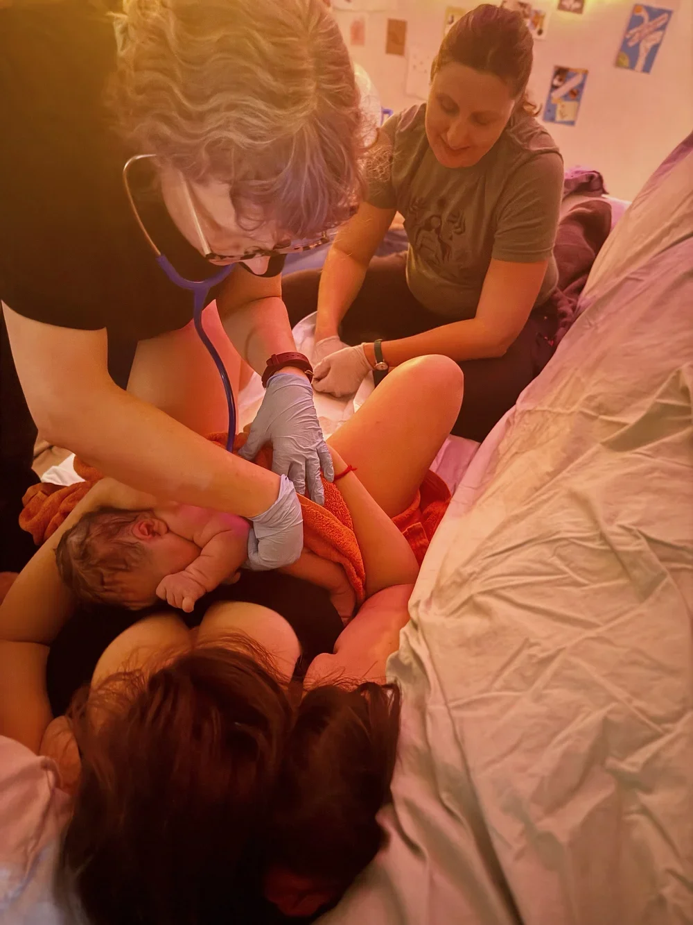Two healthcare workers midwife and doula assisting a newborn baby during delivery in a hospital room home birth with birth photographer
