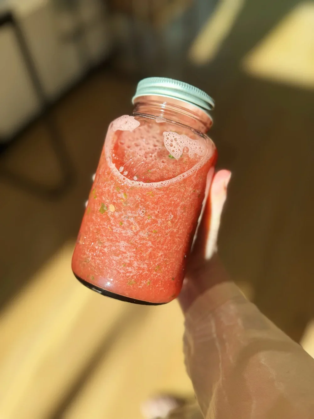 Hand holding a glass jar filled with a pink smoothie with bubbles and foam at the top.