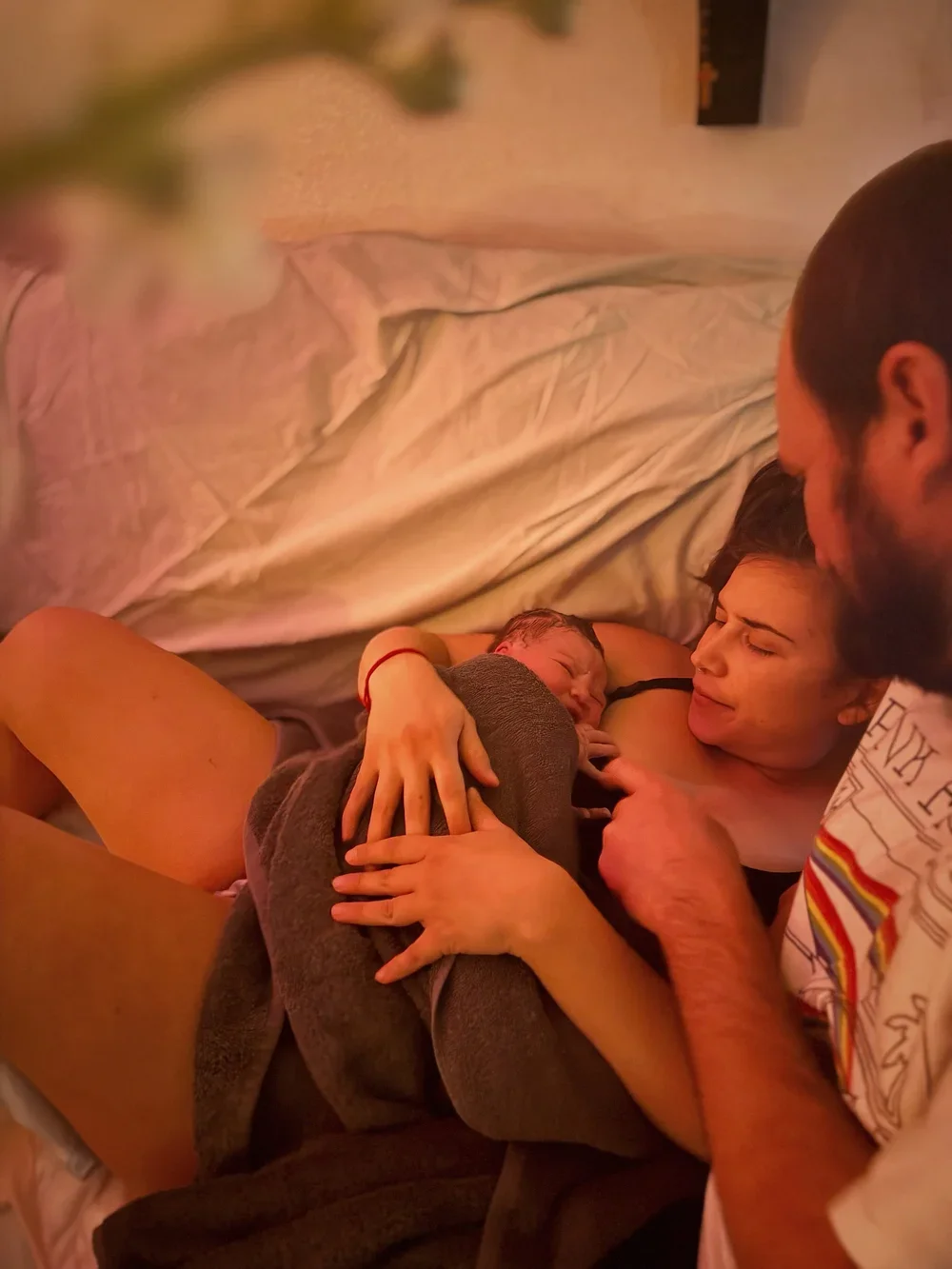 A family lying on a bed, with a woman holding a sleeping young child while a man leans in close.
