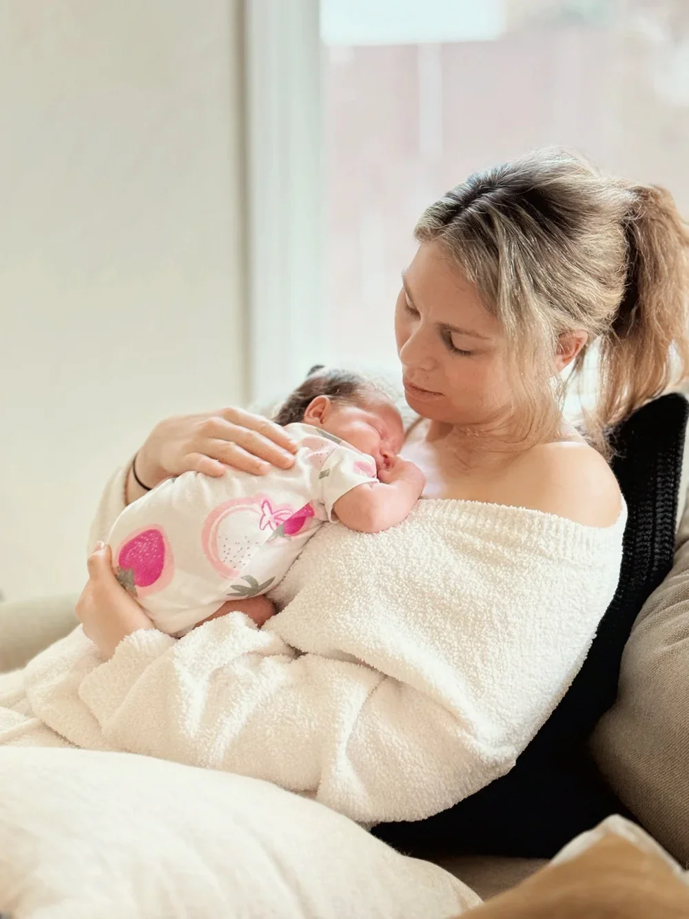 A mother holding her newborn baby on her chest, with both looking lovingly at each other in a cozy, softly lit room.