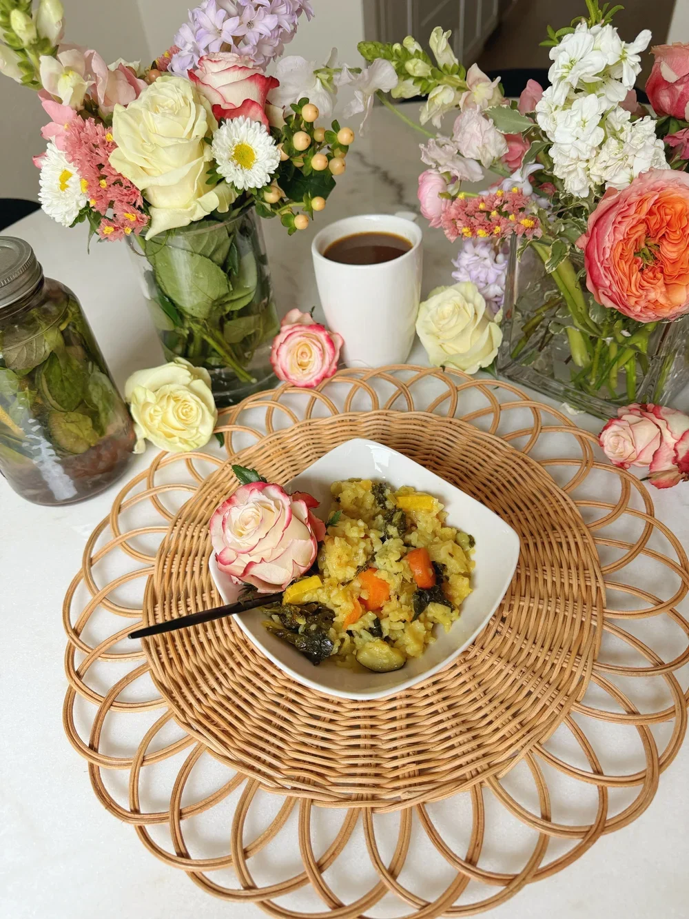 Dining table with a bowl of mashed potatoes with vegetables, a cup of coffee, and floral arrangements in vases.