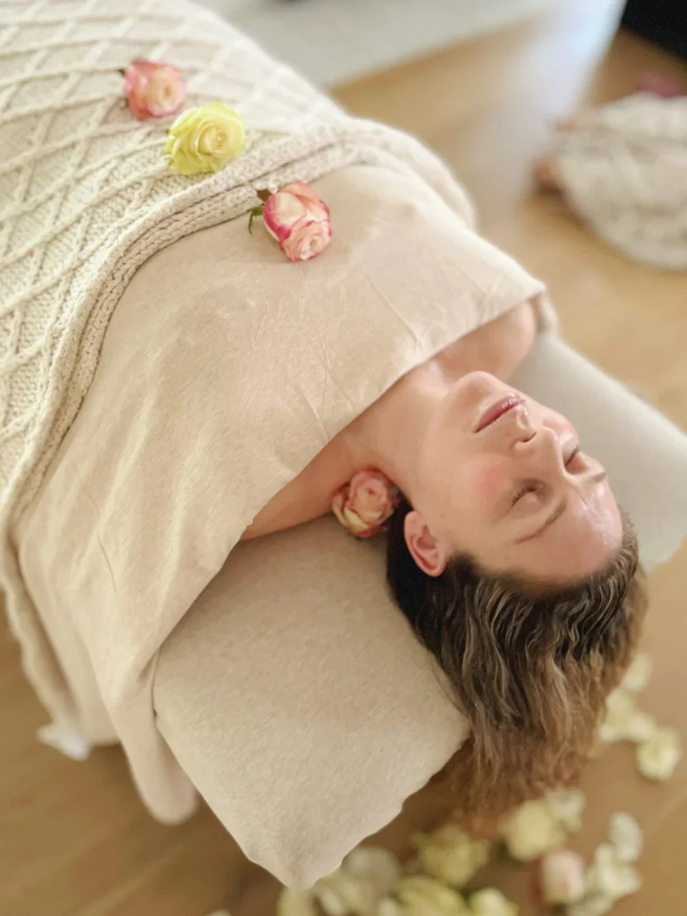 A woman lying on a massage table with her eyes closed, surrounded by pink and cream roses.