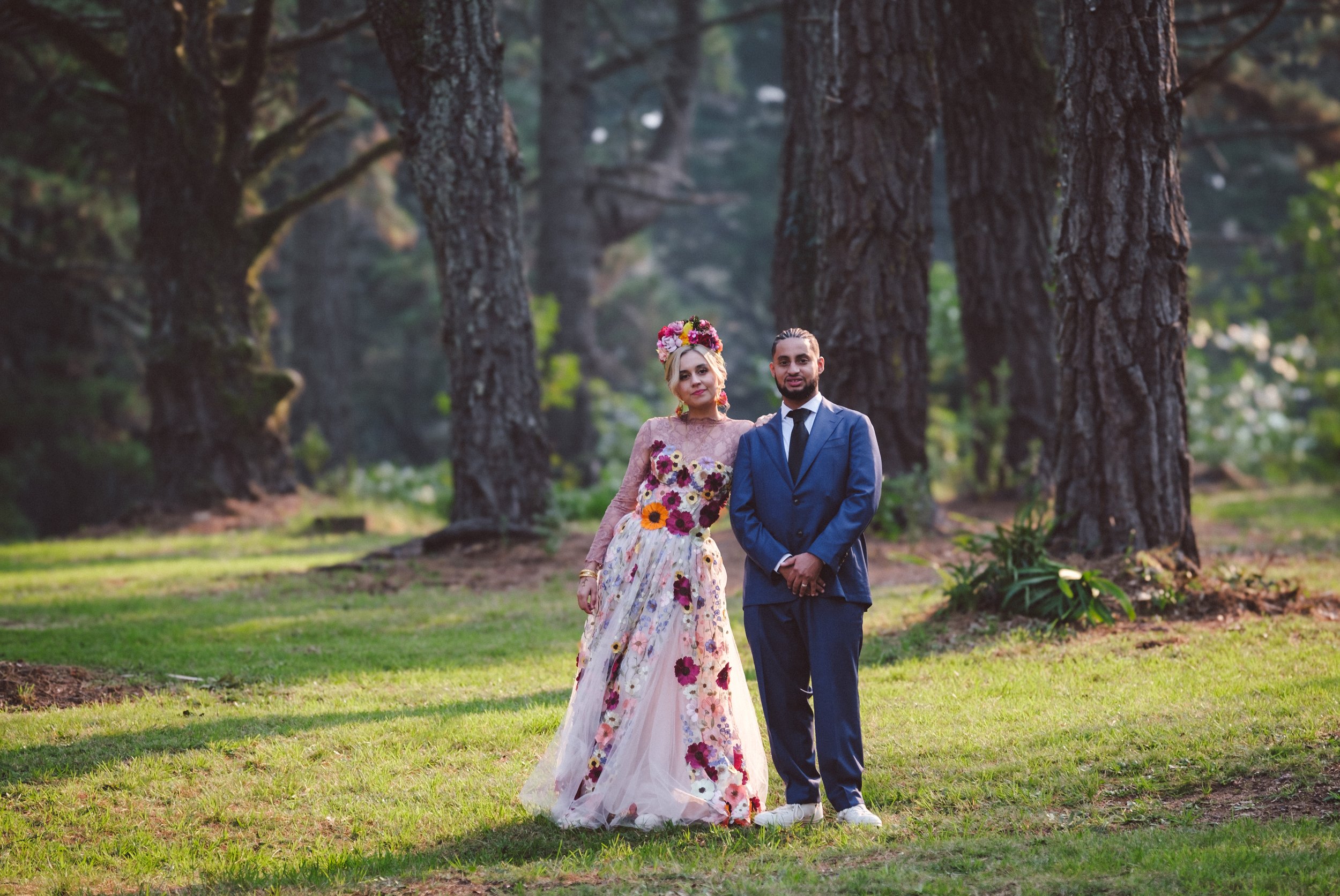 A couple stands among the trees of the Blue Mountains, the bride in a floral gown and crown — capturing the charm of a forest elopement.