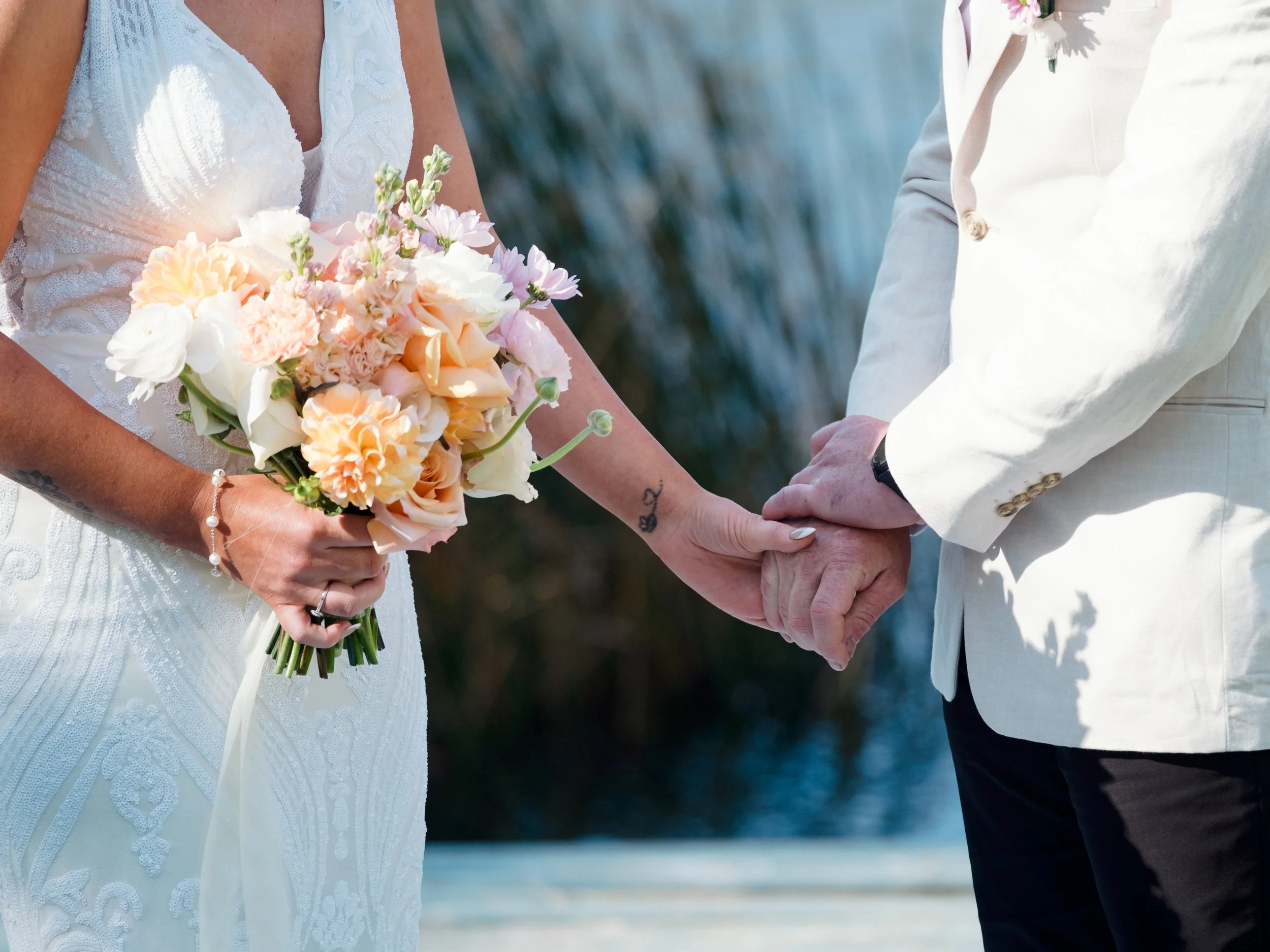 A tender close-up of a couple holding hands during their Blue Mountains elopement, with a pastel bouquet symbolizing their union.