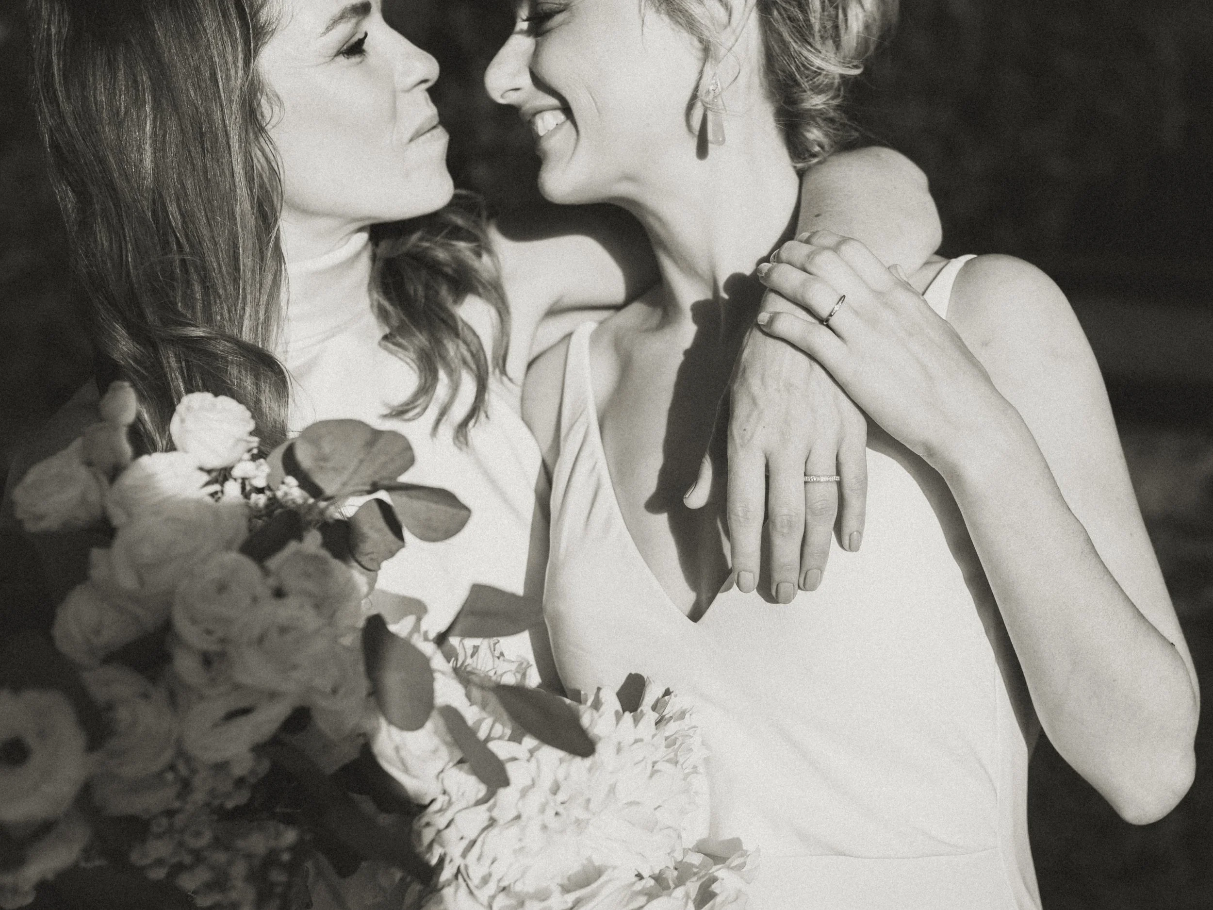 Two women celebrate their Blue Mountains elopement with a joyful embrace, holding flowers and smiling in a moment of pure connection.