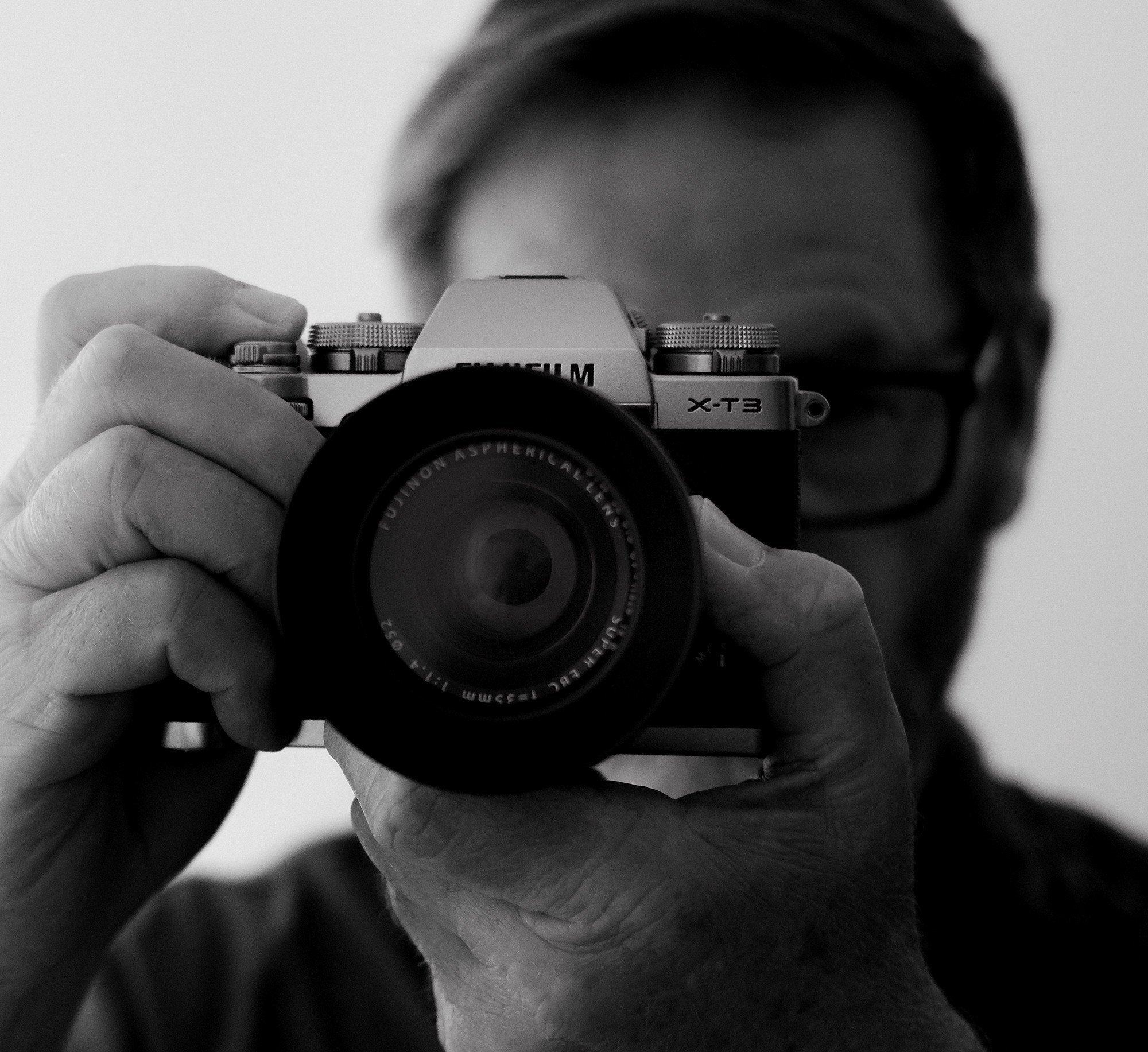 A person taking a photo with a camera, positioned in front of their face, in black and white.