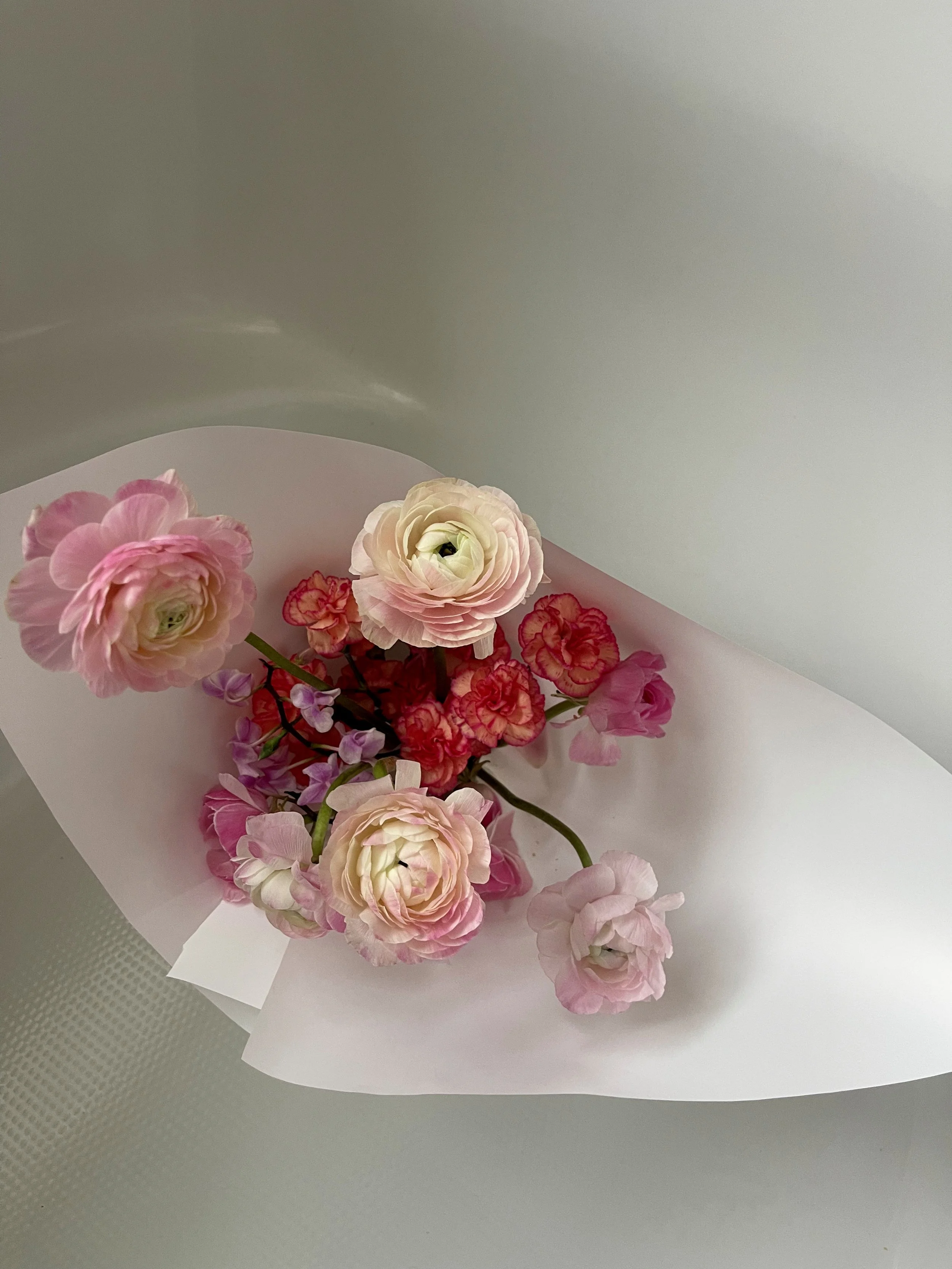A bouquet of pink and white flowers wrapped in white paper.