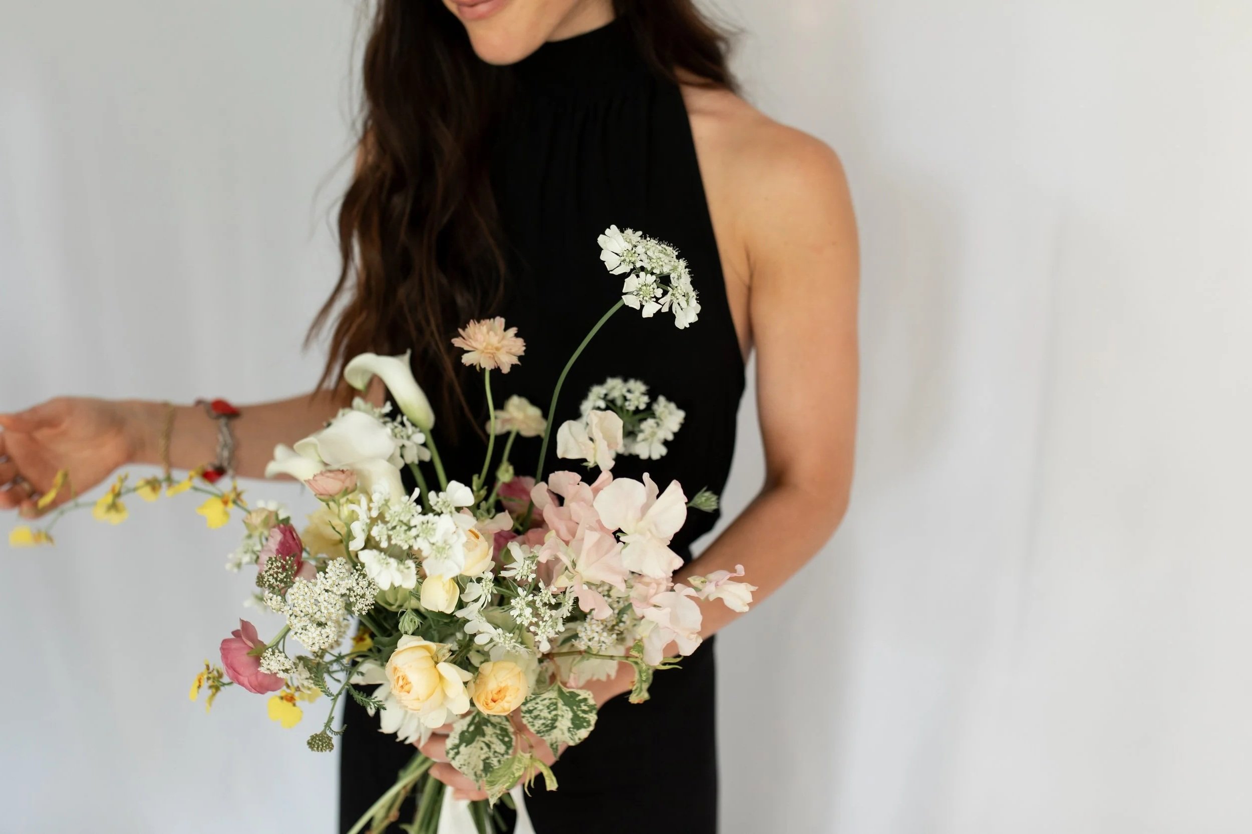 Woman in a black halter dress holding a bouquet of mixed pastel-colored flowers
