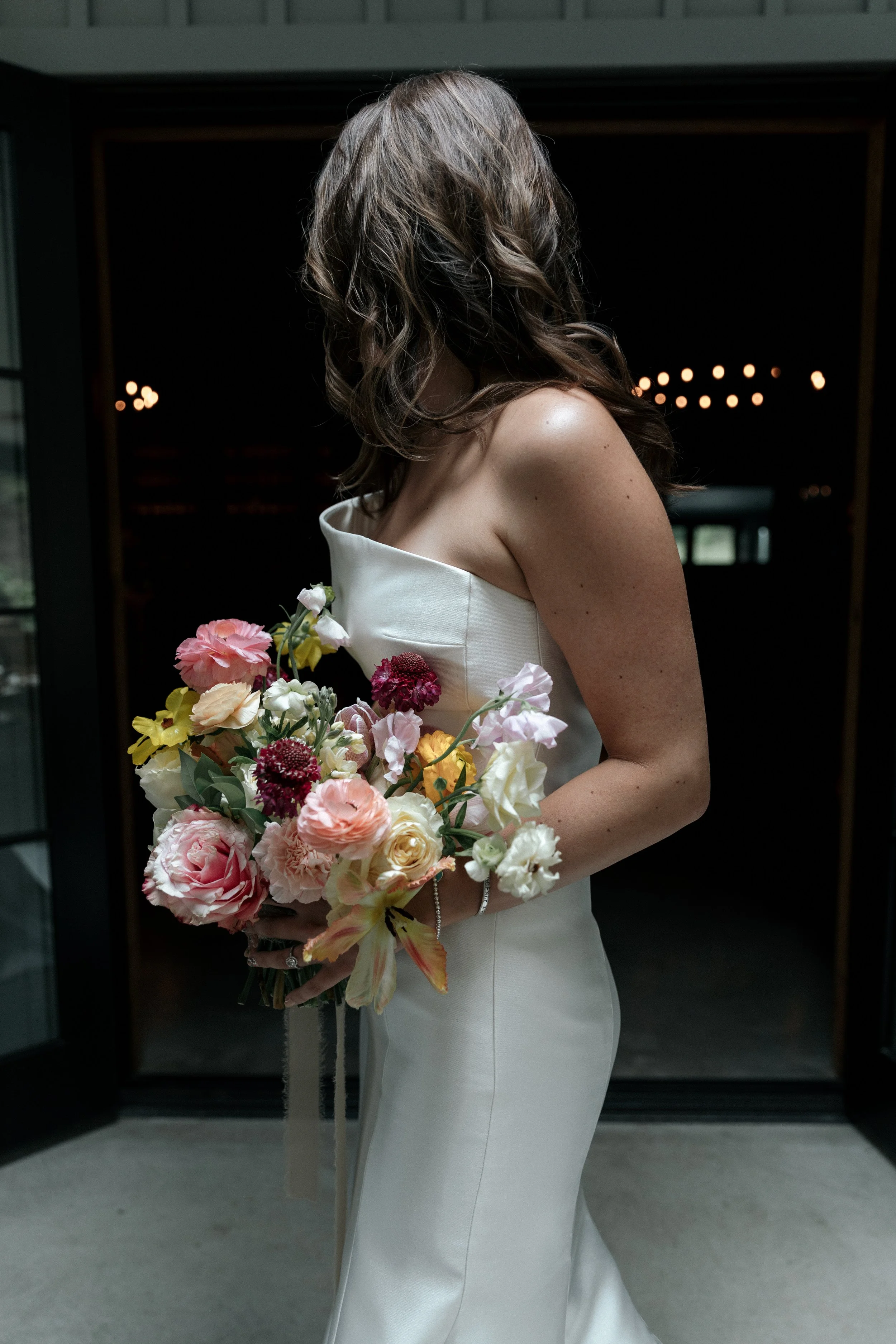 A woman in a white strapless dress holding a colorful bouquet of flowers.