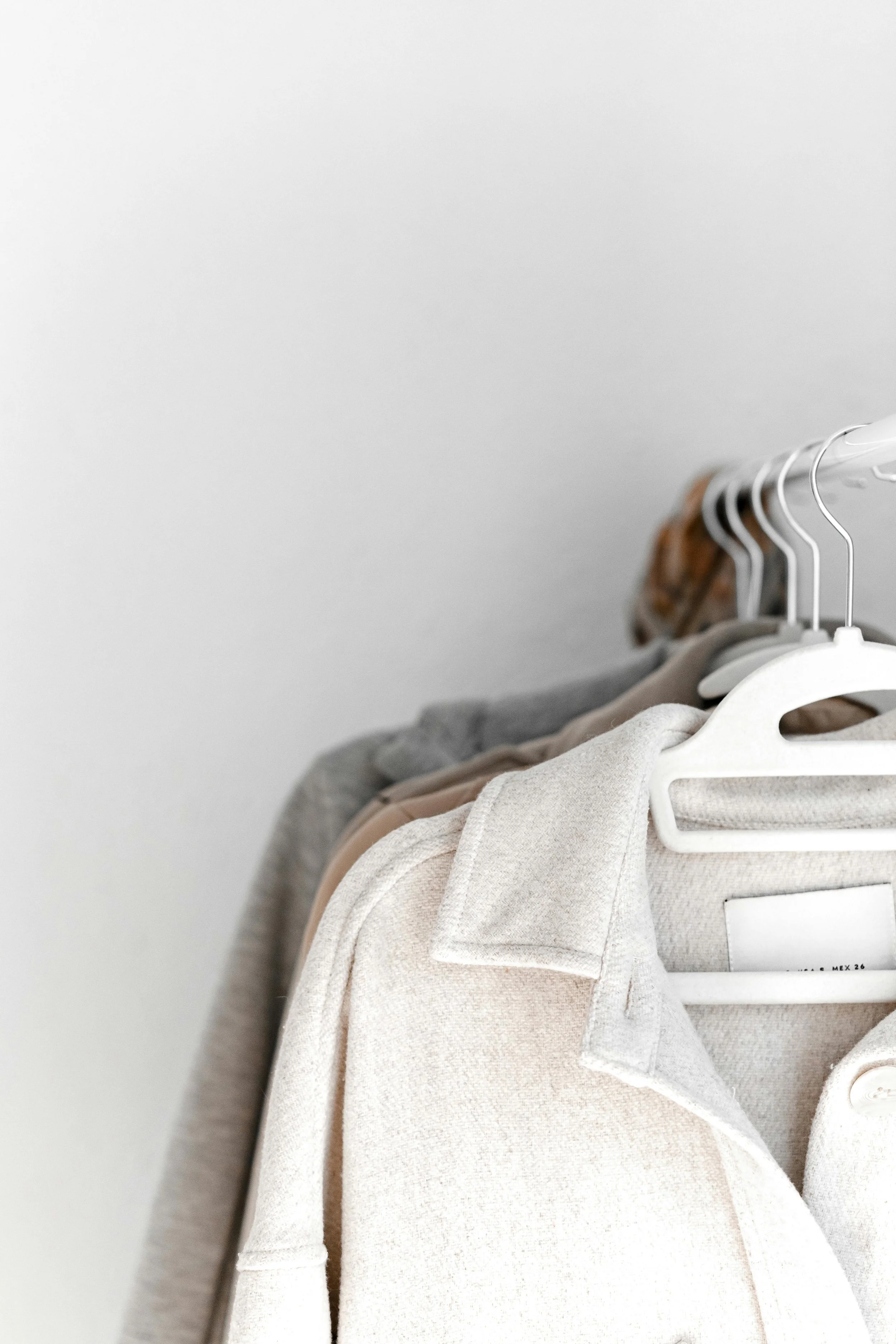 Close-up of a beige coat hanging on a rack with other clothing items in the background.