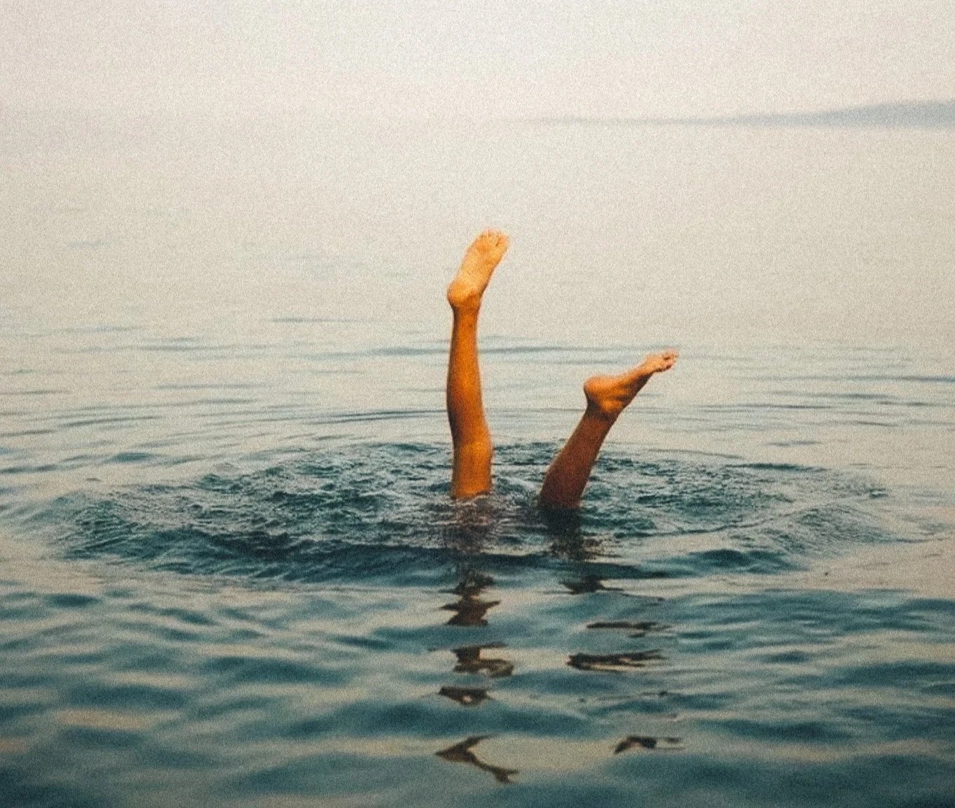 Due gambe emergono dall'acqua, con uno che si alza e l'altro che si inclina, in un mare calmo con un cielo limpido.
