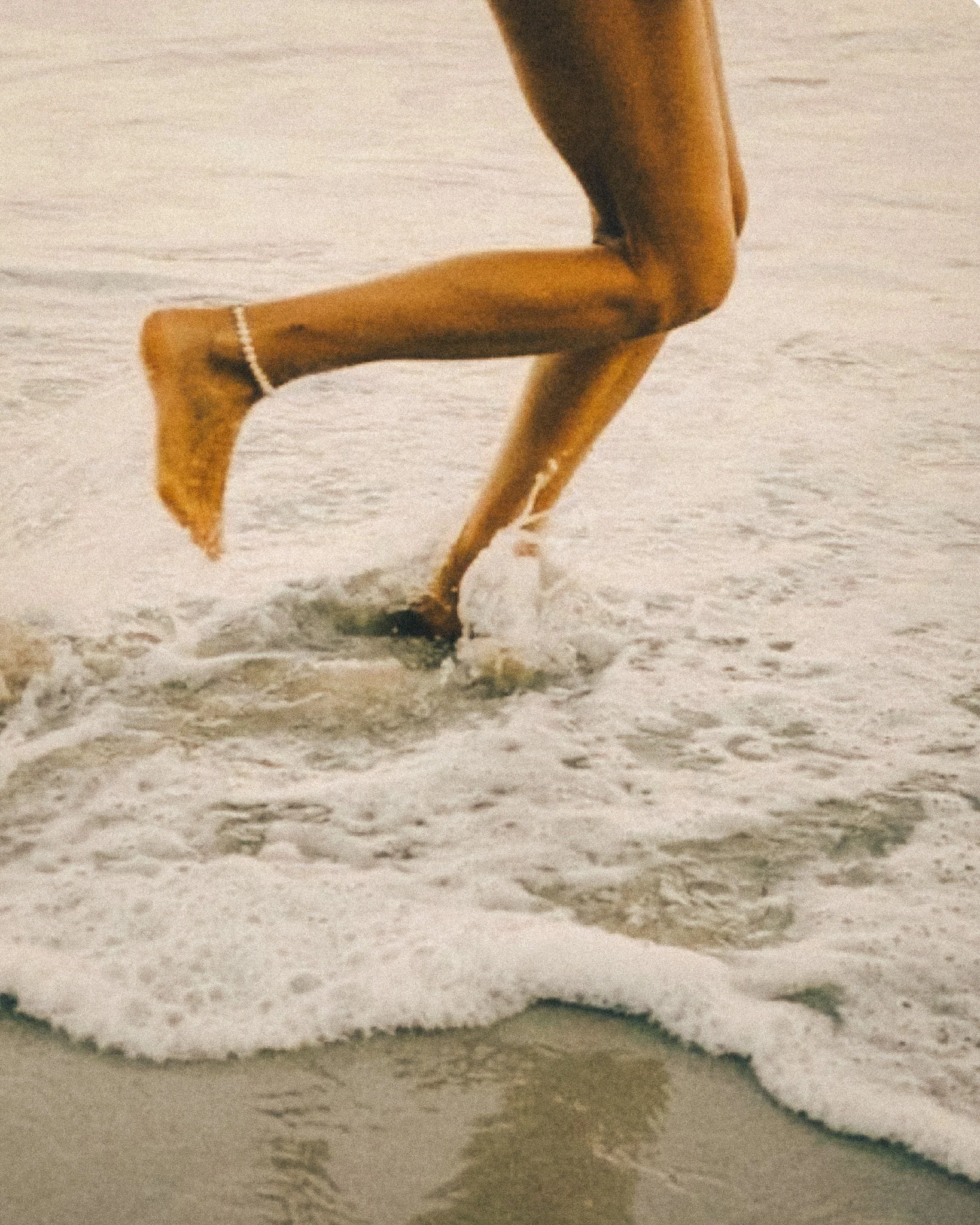 Una persona che corre sulla spiaggia con il mare e le onde che si infrangono ai suoi piedi.
