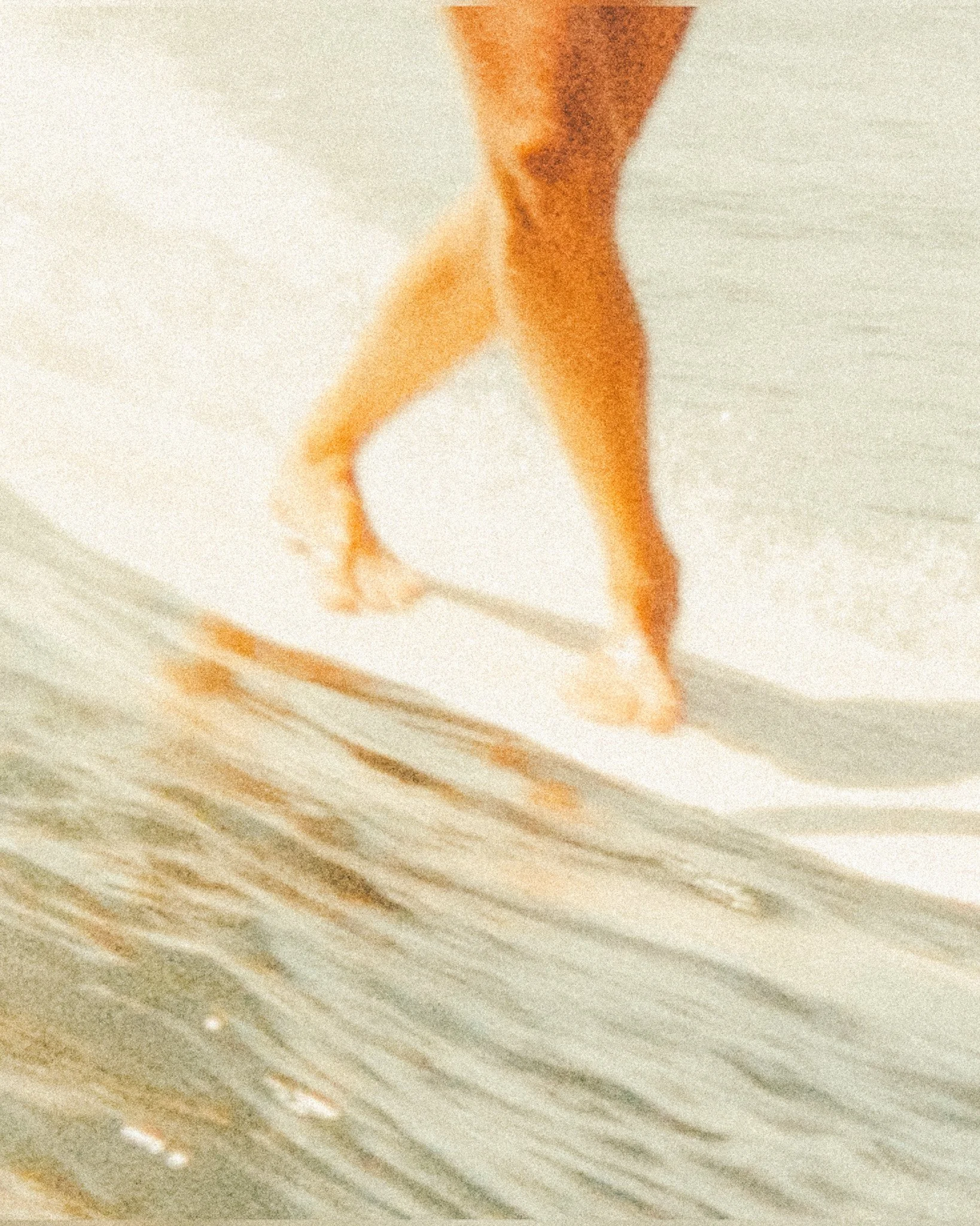 Piedi di una persona che cammina sulla riva del mare, con le onde che lambiscono la spiaggia