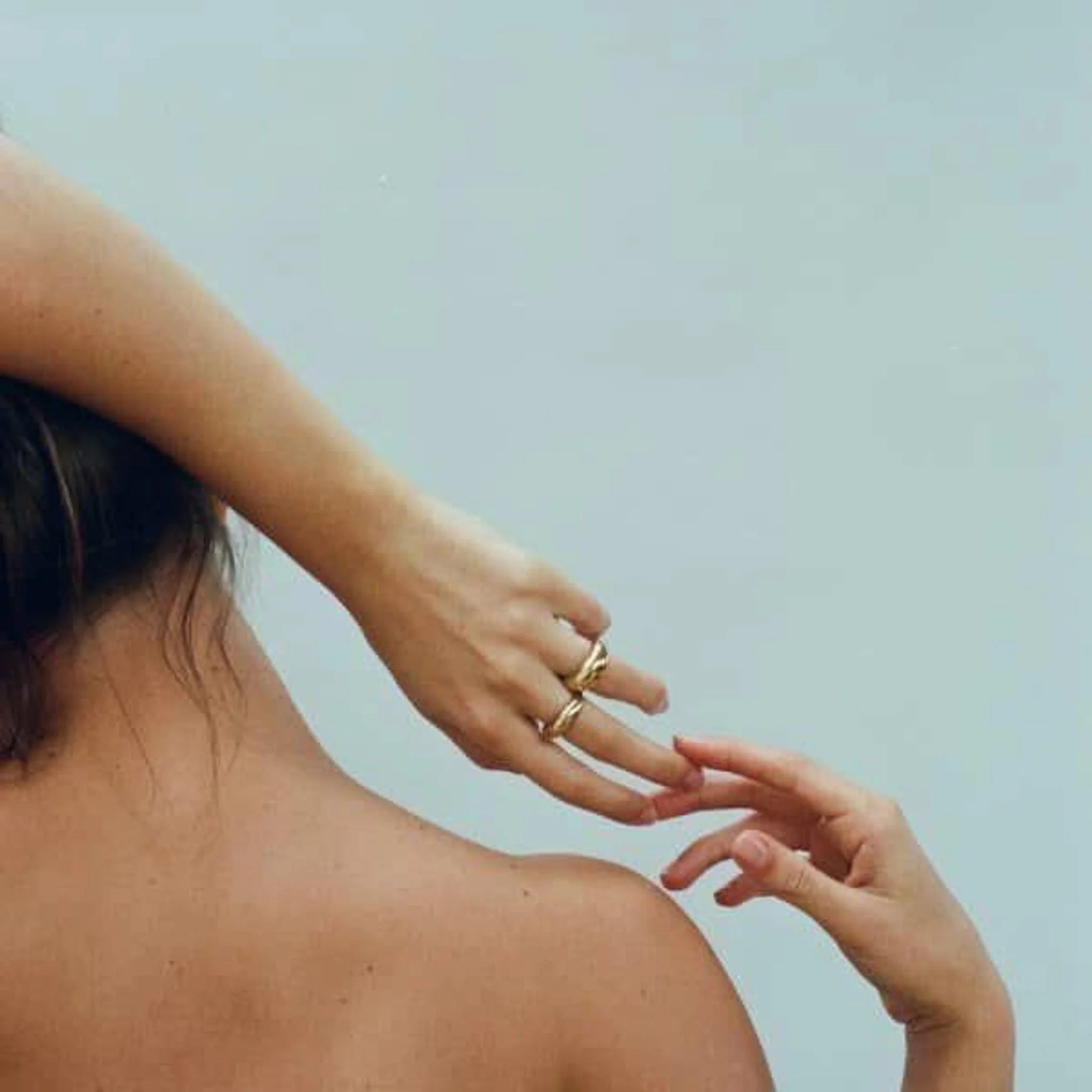 Due mani che si sfiorano con le dita, una delle mani è legata ad un braccio e una spalla nuda di una persona con pelle chiara, sfondo bianco.