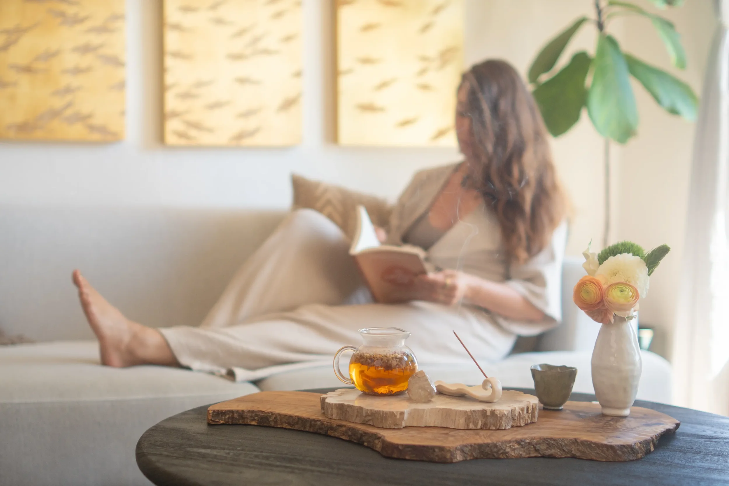ARAMTALA home goods brand launch lifestyle scene with tea, incense, flowers and a woman reading.