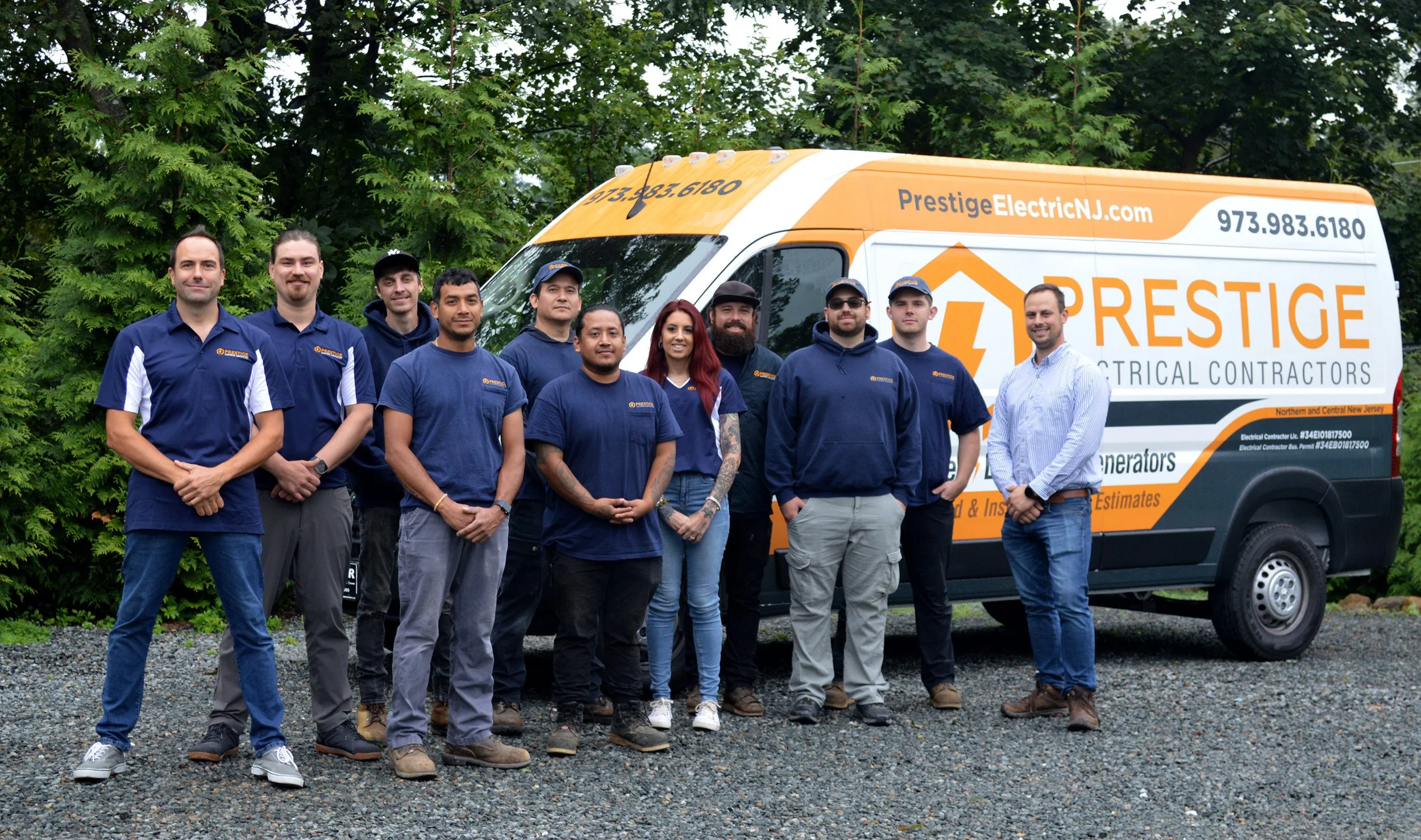 Group of electrical contractors standing outdoors next to a company van with orange and white branding for Prestige Electric NJ.